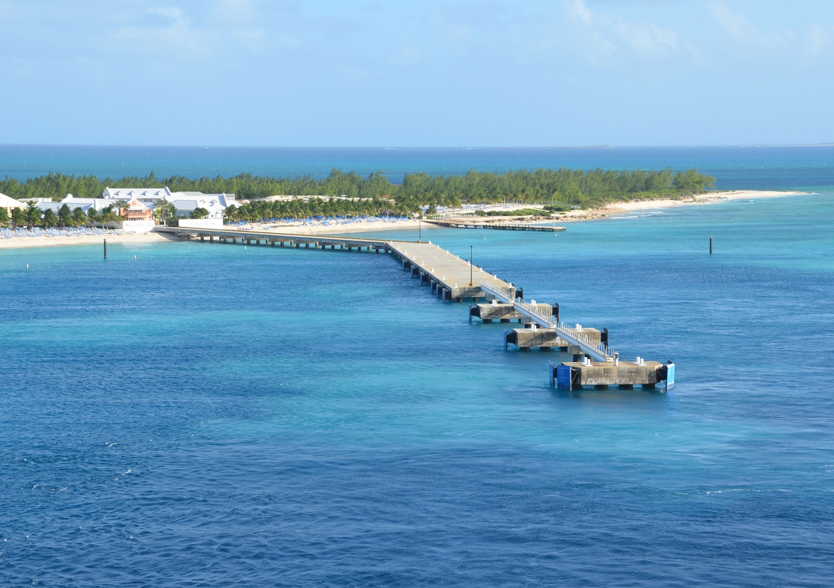Grand Turk cruise pier extending into clear turquoise waters, with a sandy beach and resort facilities in the background.