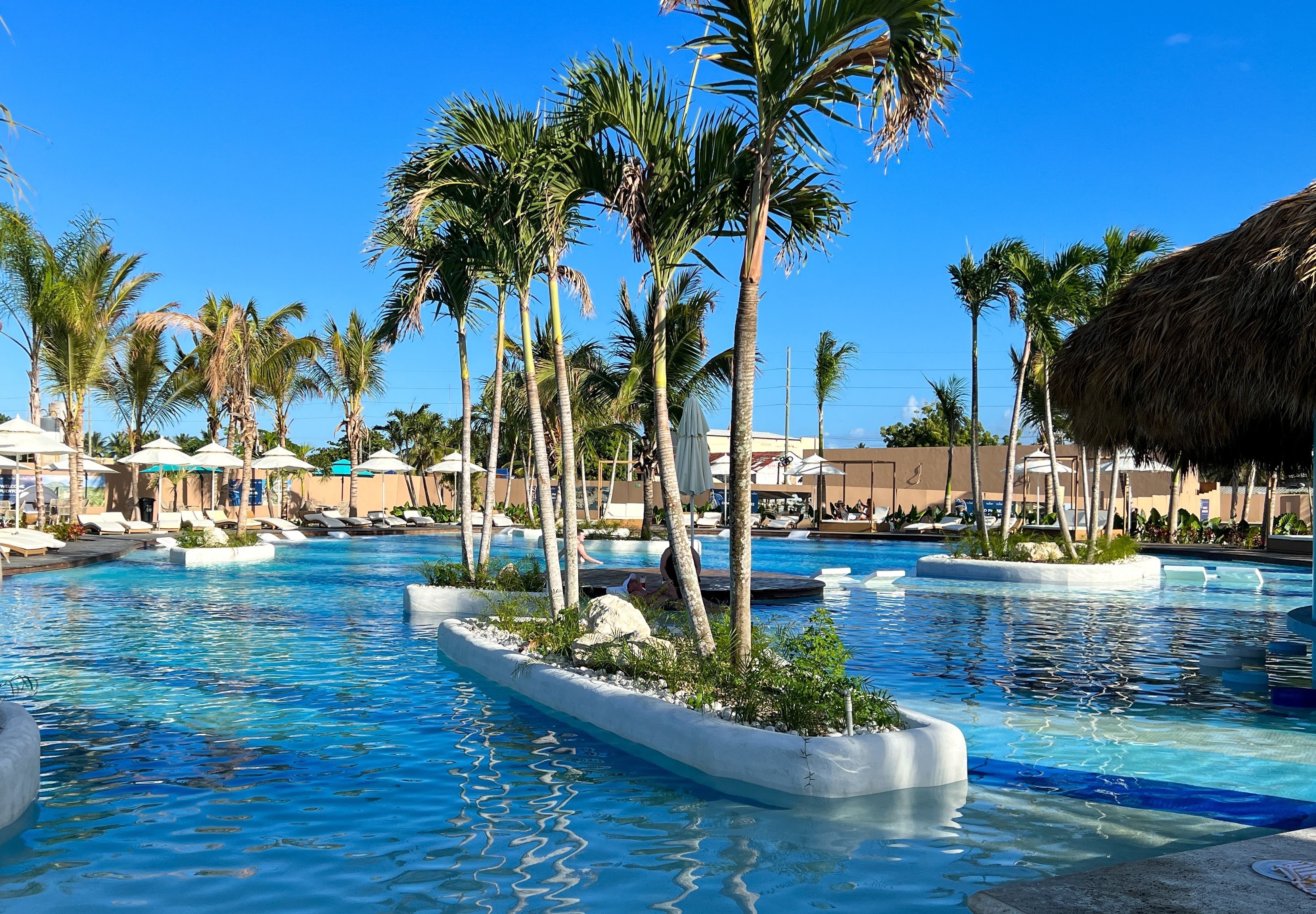 Lush pool area at Taino Bay in Puerto Plata, Dominican Republic, with palm trees, sun loungers, and crystal-clear water.
