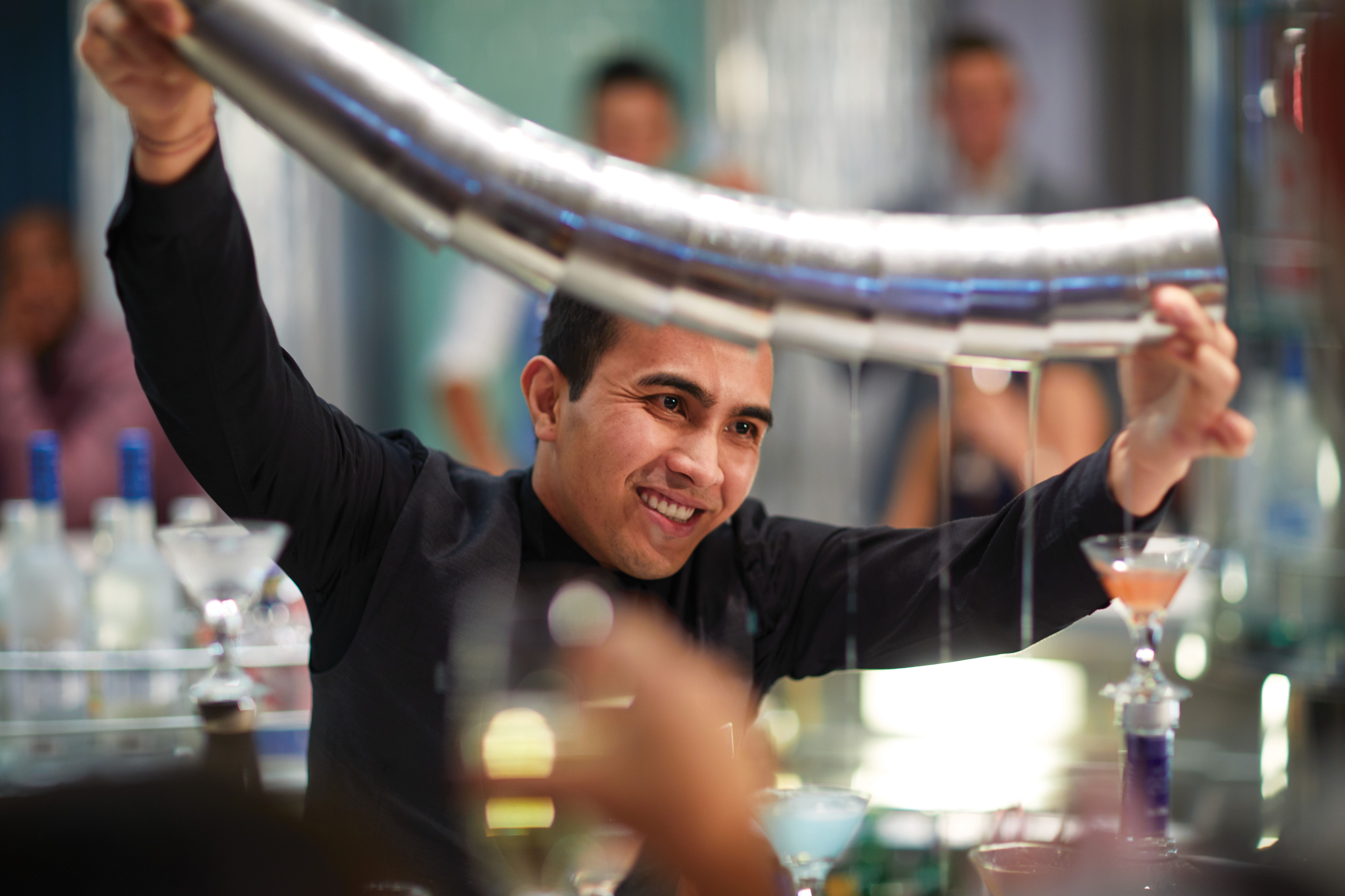 Bartender performing a flair pour at the Martini Bar on a cruise ship, with cocktails and a lively atmosphere.