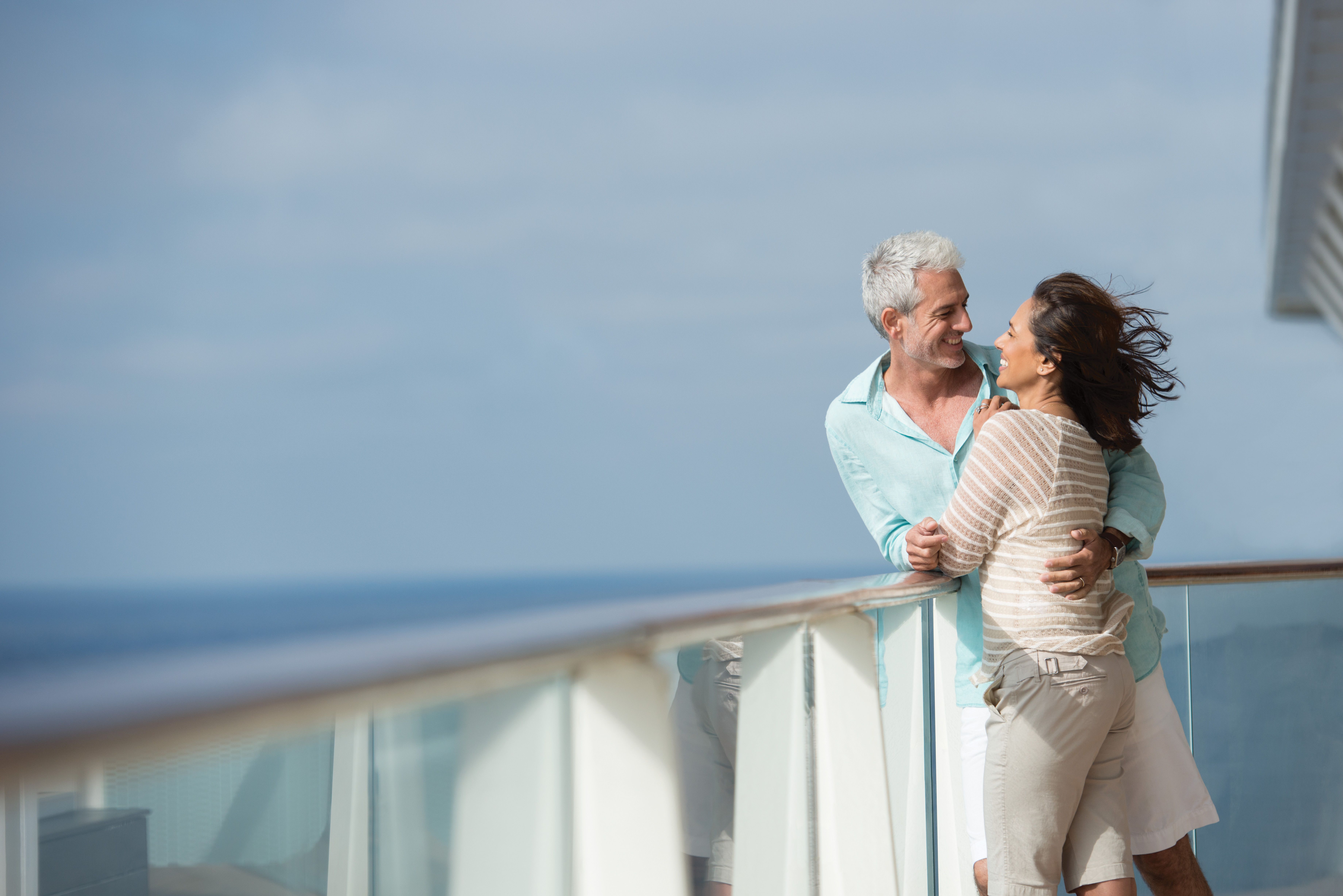 Couple embracing on a private penthouse suite balcony aboard a cruise ship, enjoying ocean views and sea breeze under clear skies.