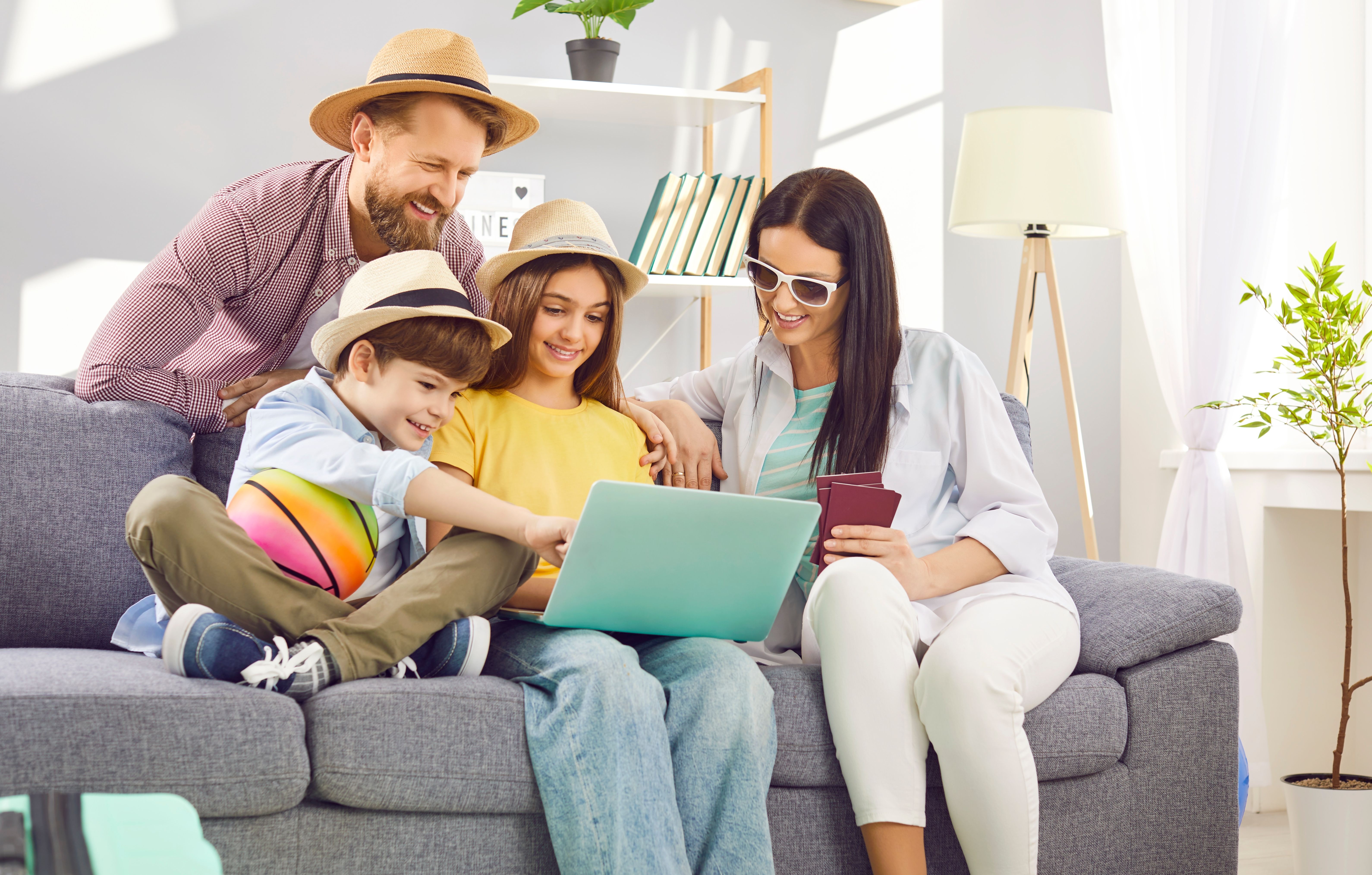 Happy family in vacation outfits booking a cruise online at home, holding passports and planning their getaway together.