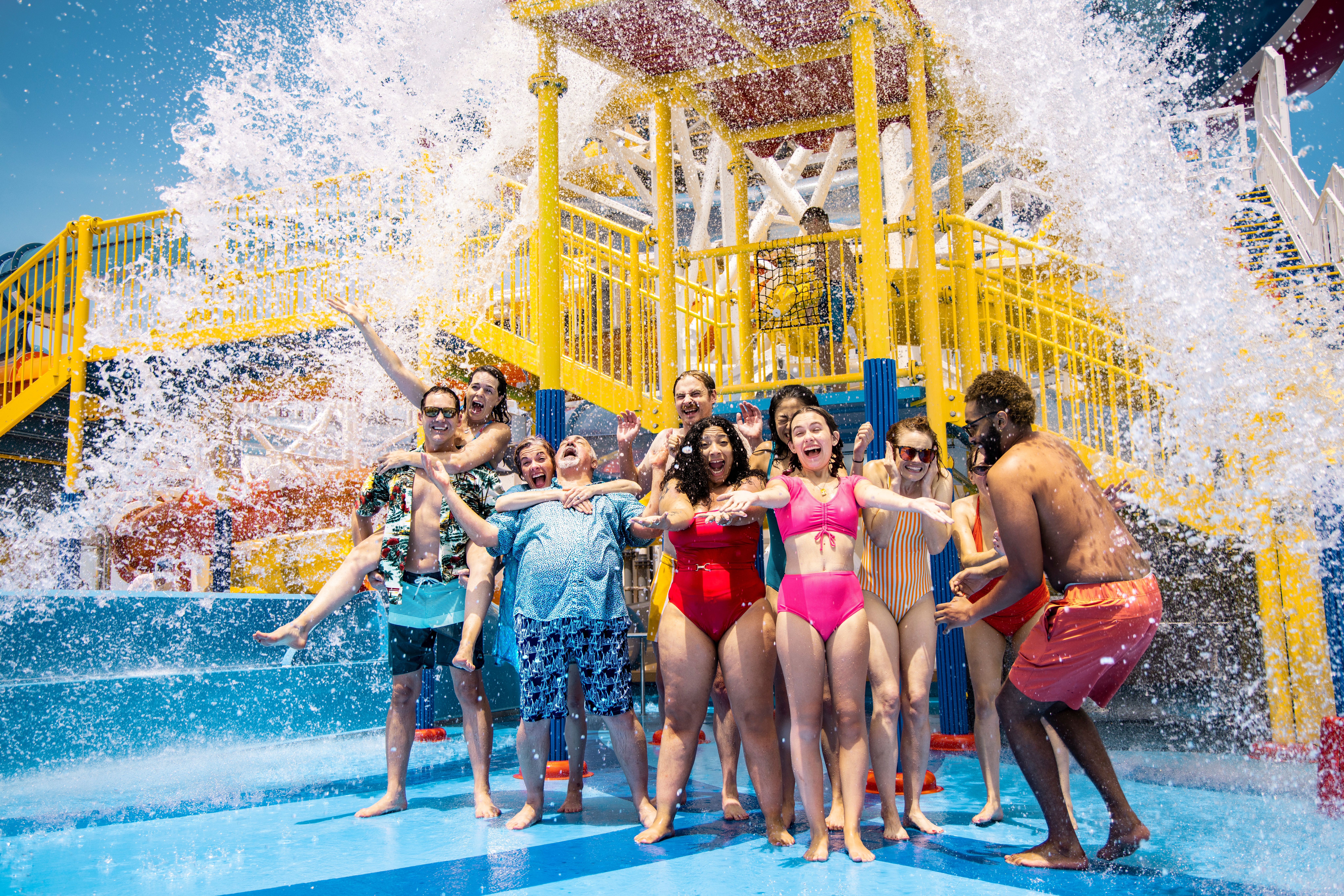Guests laugh under a giant splash at WaterWorks on Carnival Mardi Gras, surrounded by bright slides and colorful water play structures under sunny skies.