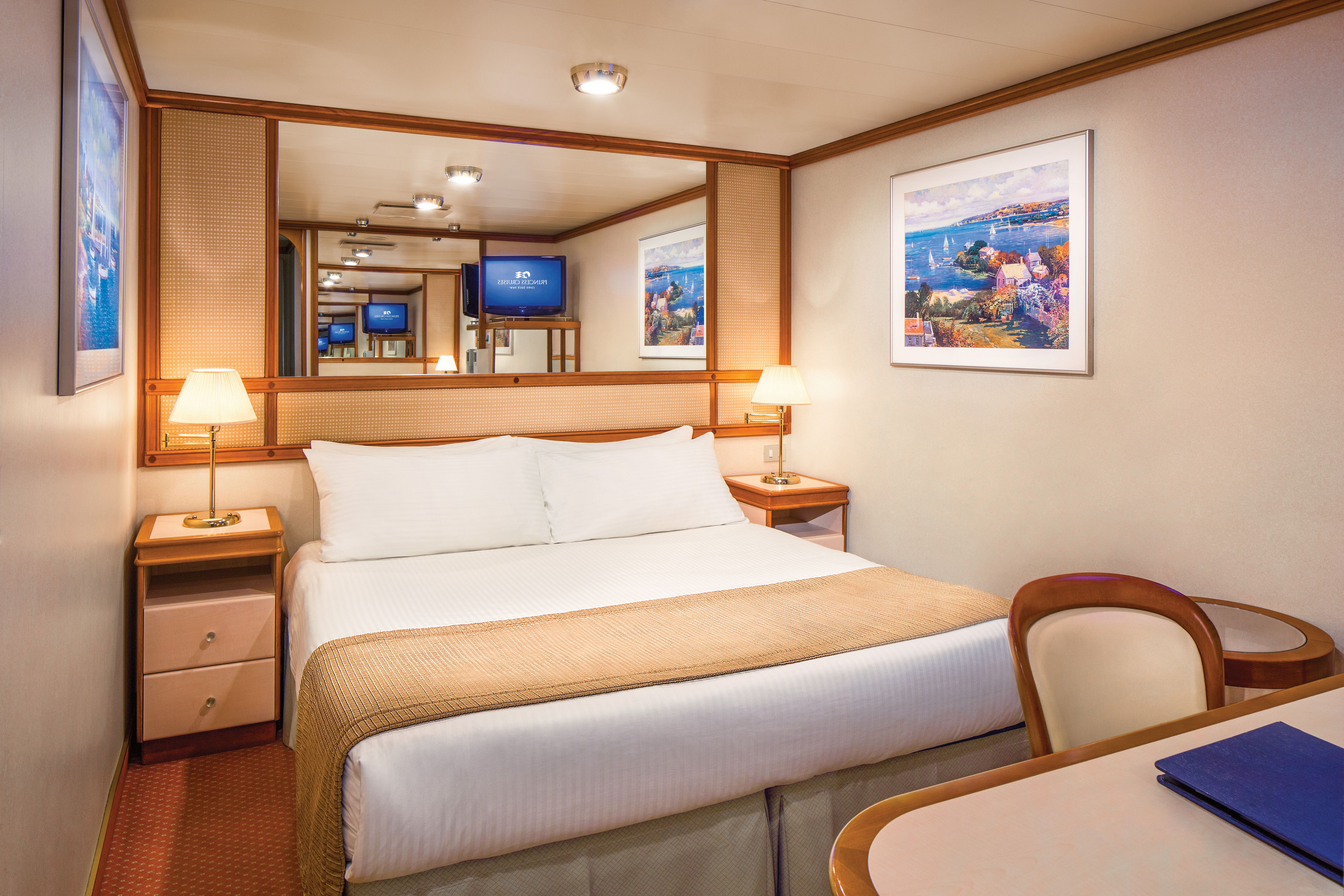 Interior stateroom on Princess Cruises with queen bed, warm lighting, desk, TV, and artwork—cozy and elegant for restful nights at sea.