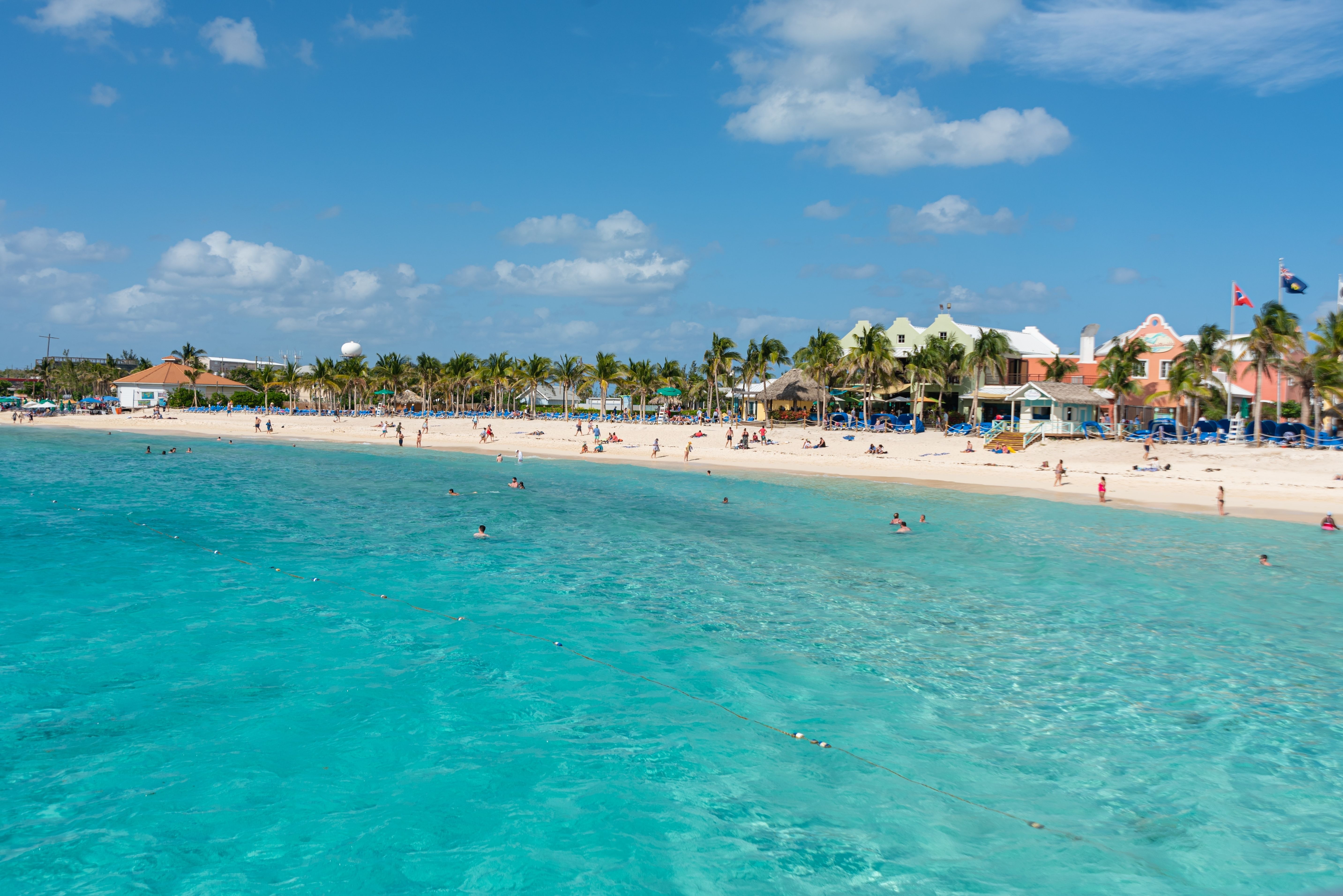 Grand Turk beach with clear turquoise waters, palm trees, and pastel-colored shops, popular cruise port destination in the Turks and Caicos Islands.
