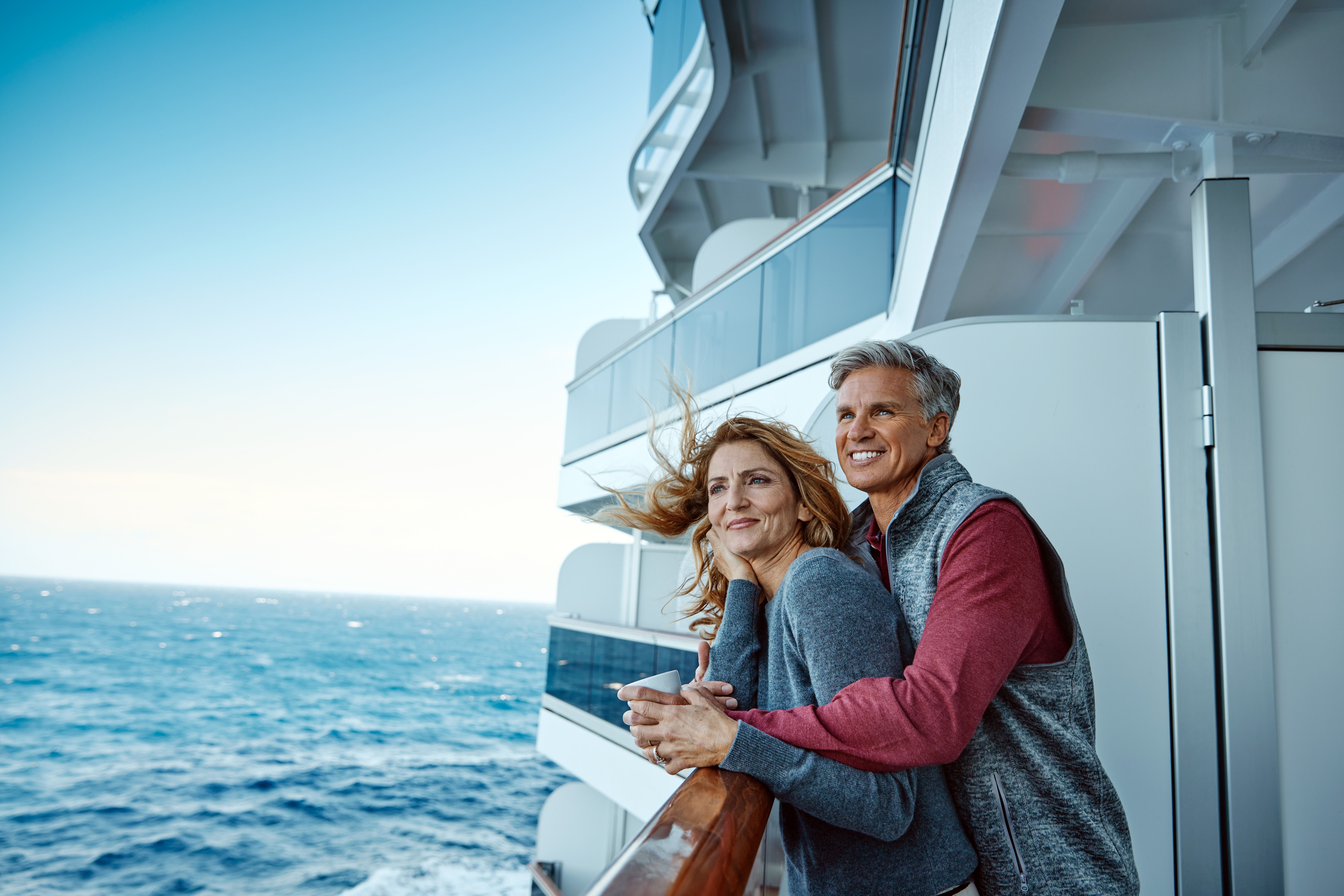Senior couple enjoys ocean views from private verandah on Neptune Suite balcony aboard Holland America cruise ship.