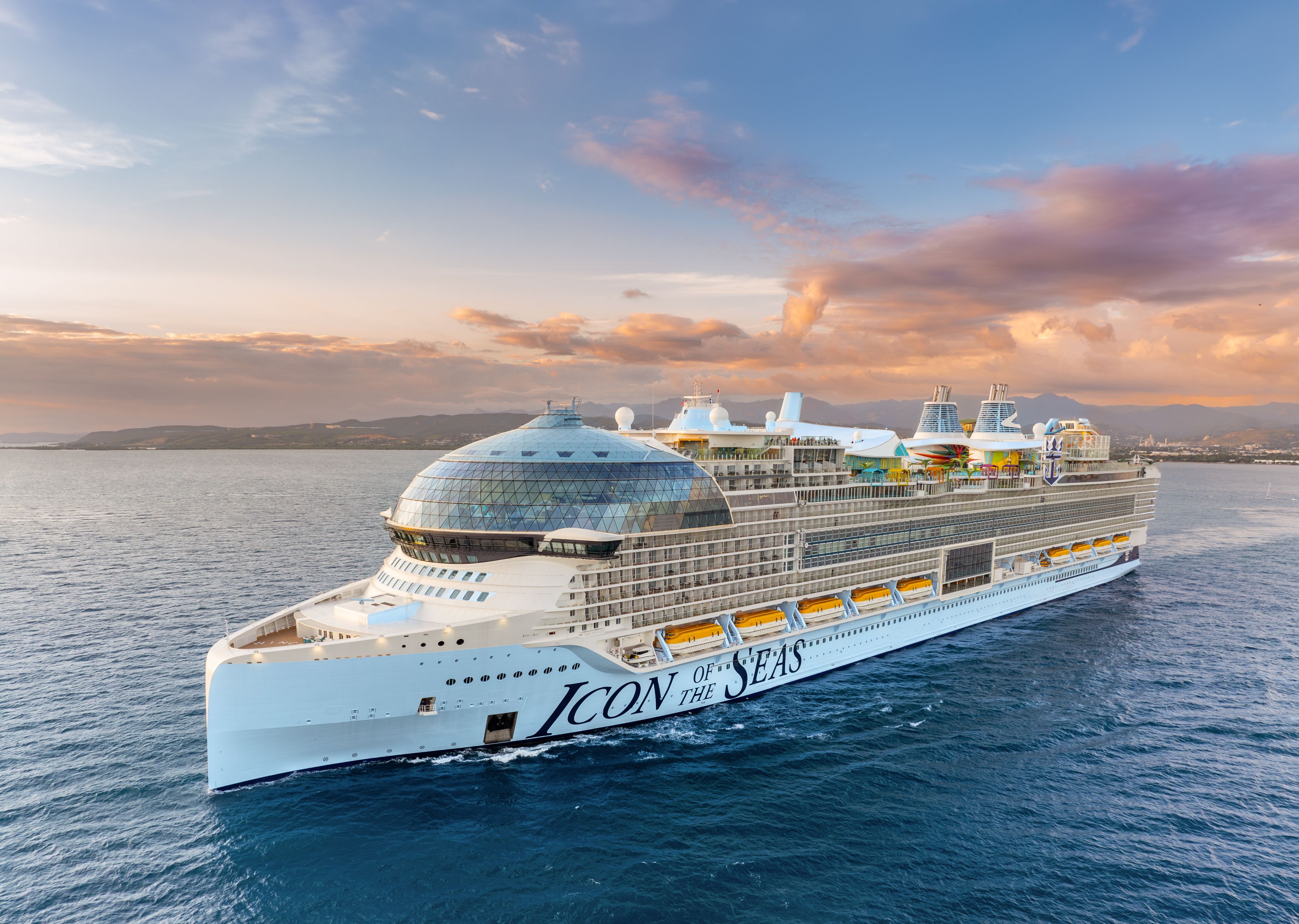 Royal Caribbean's Icon of the Seas sailing at sunset, showcasing largest cruise ship with glass dome and colorful decks.
