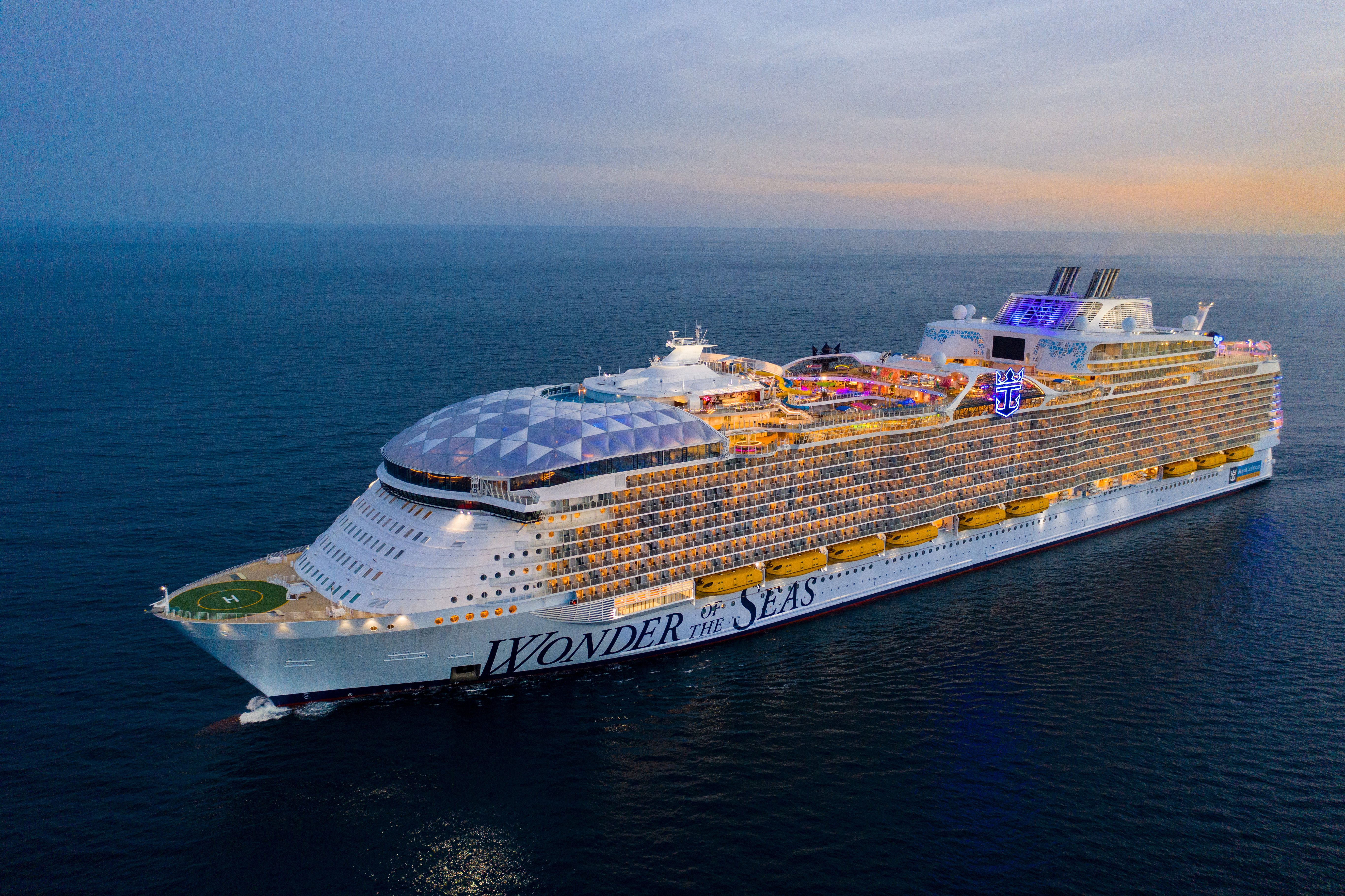 Royal Caribbean's Wonder of the Seas illuminated at dusk, world's largest cruise ship sailing through open ocean.