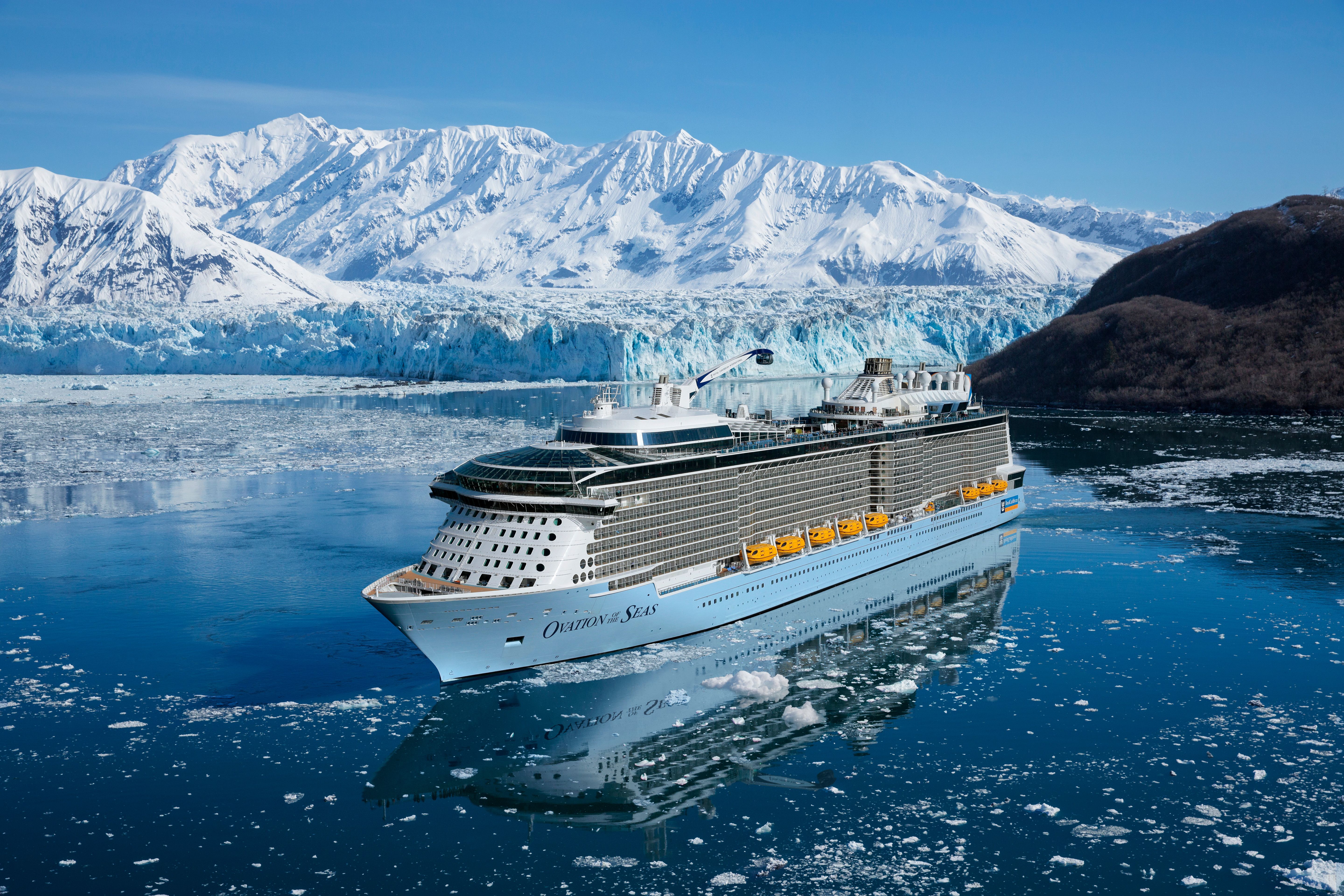 Royal Caribbean's Ovation of the Seas cruising through icy Alaskan waters with glacier and snow-covered mountains in background.