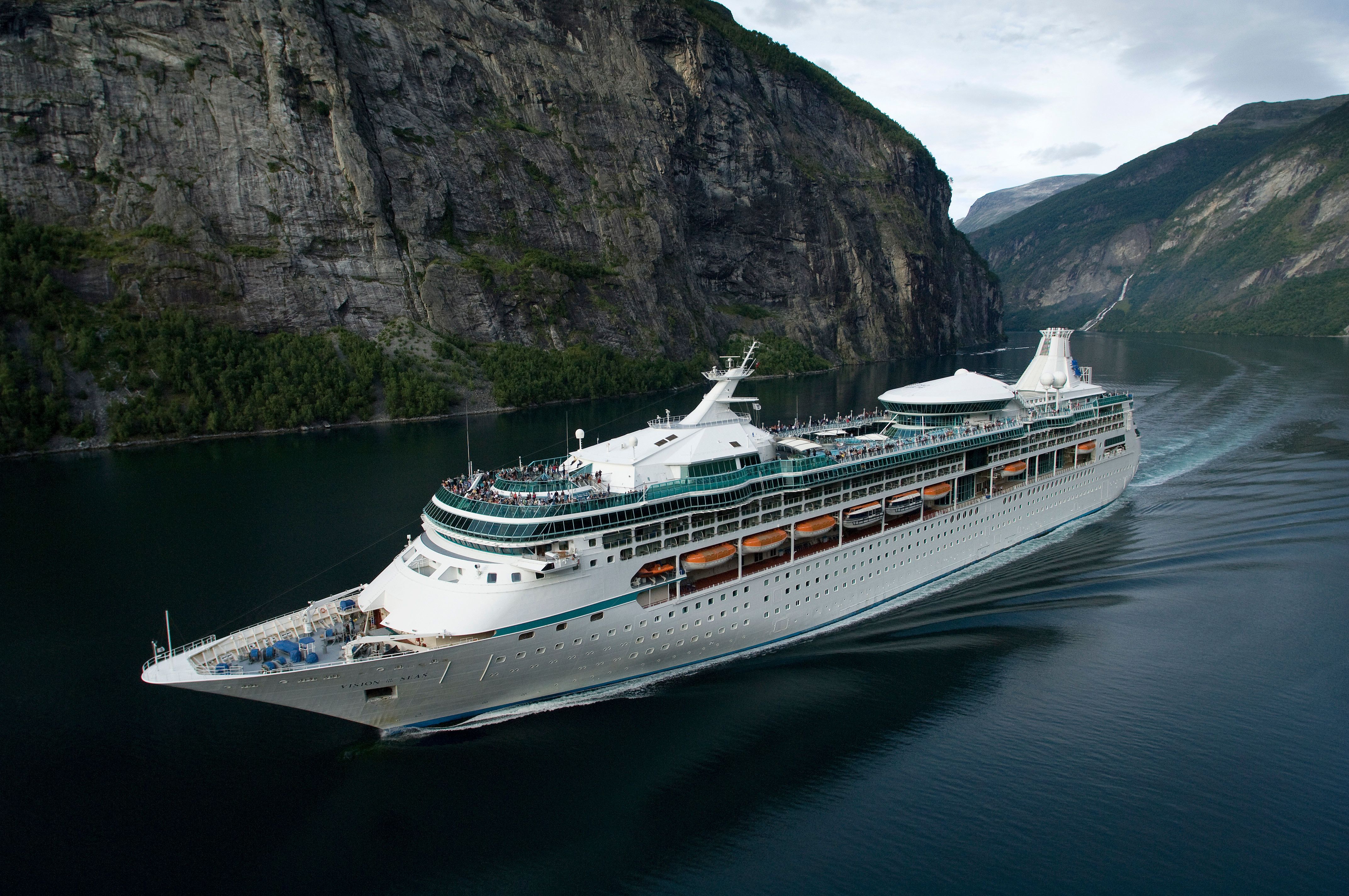 Royal Caribbean’s Vision of the Seas cruising through Norway’s fjords, surrounded by steep cliffs and serene green waters.