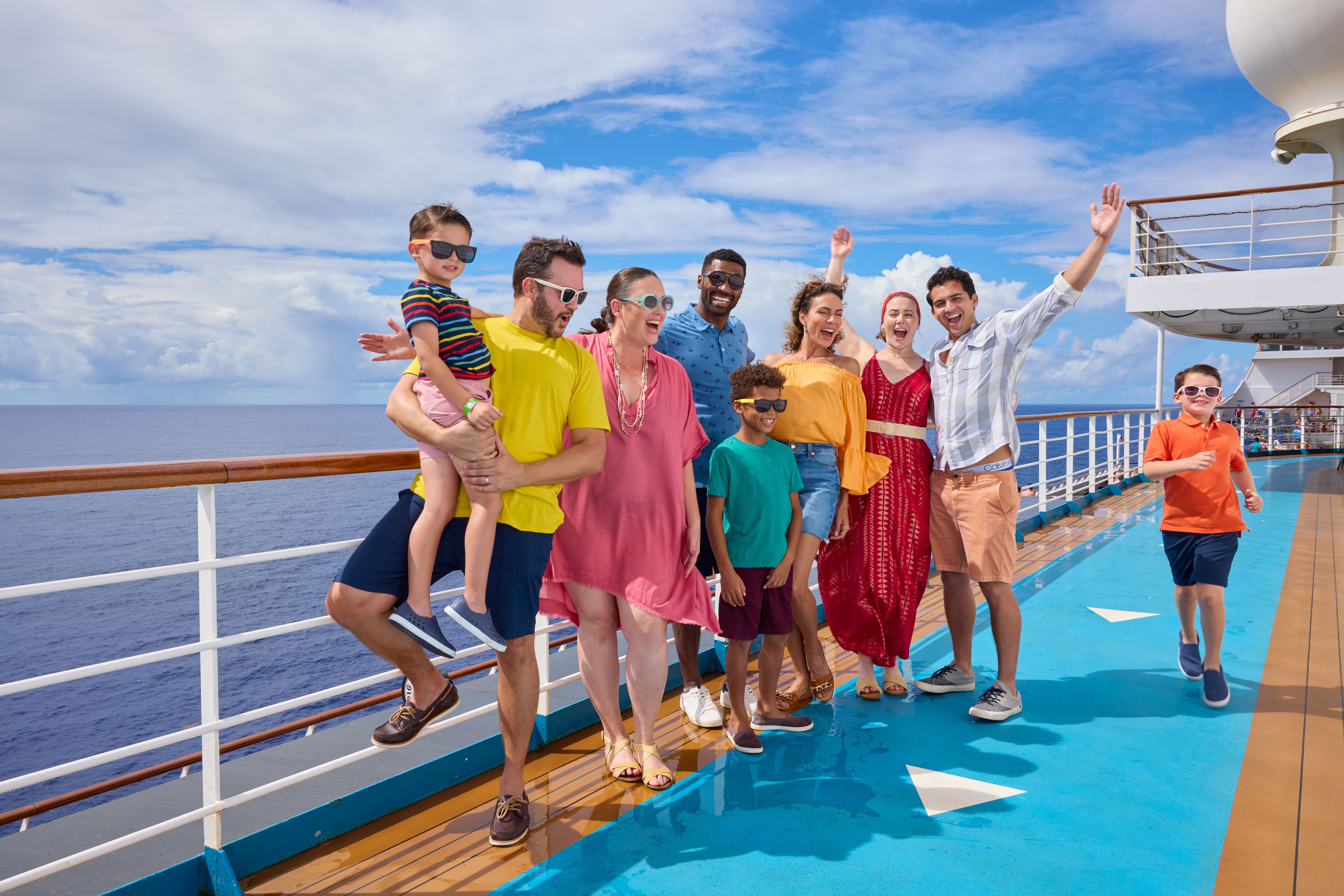 Multigenerational family enjoying sunny day on Carnival cruise ship deck, smiling and wearing bright outfits with ocean views behind them.