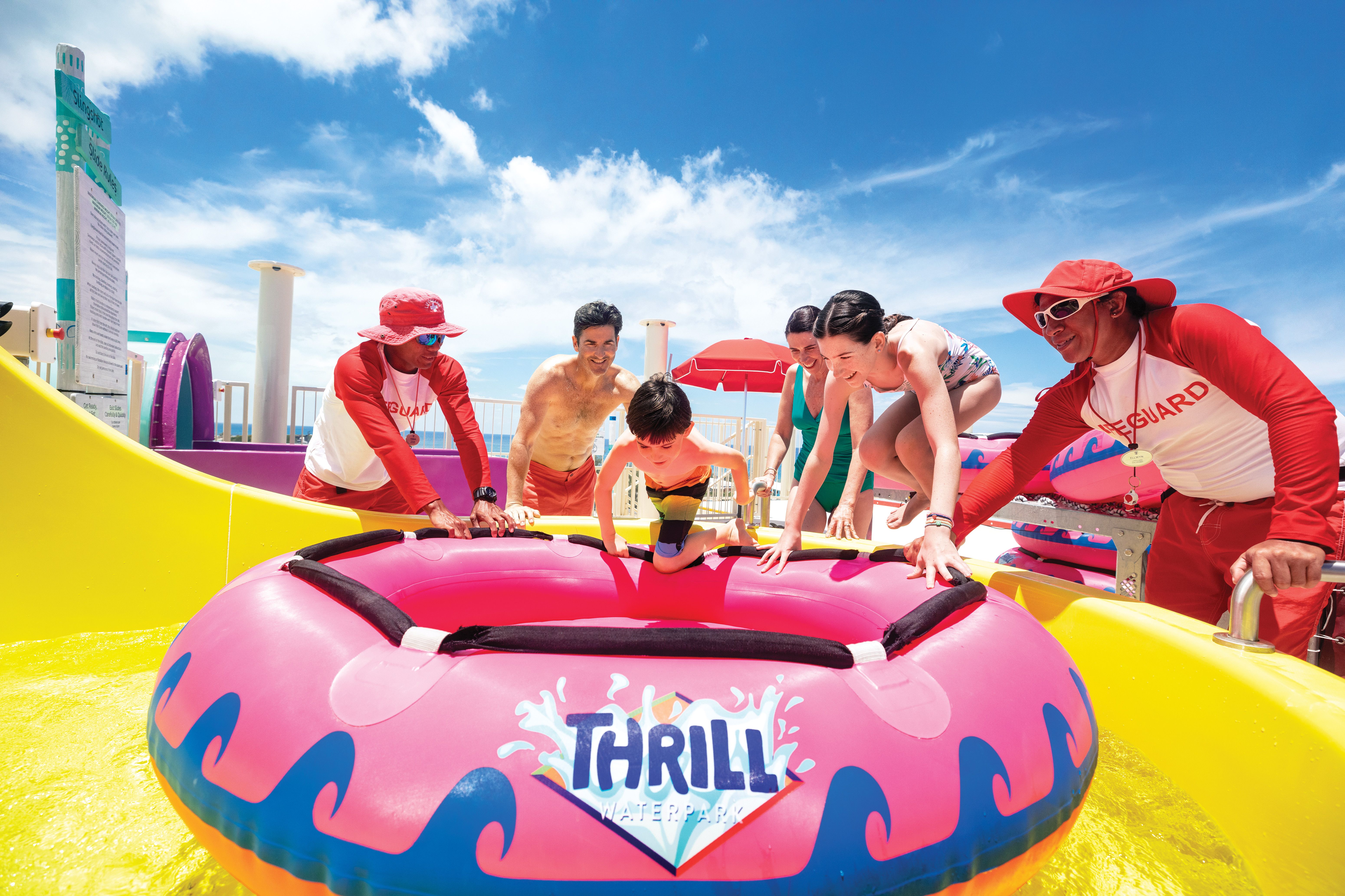 Family climbing into pink raft at Thrill Waterpark at Perfect Day at CocoCay, with lifeguards and bright waterslides under sunny blue skies.