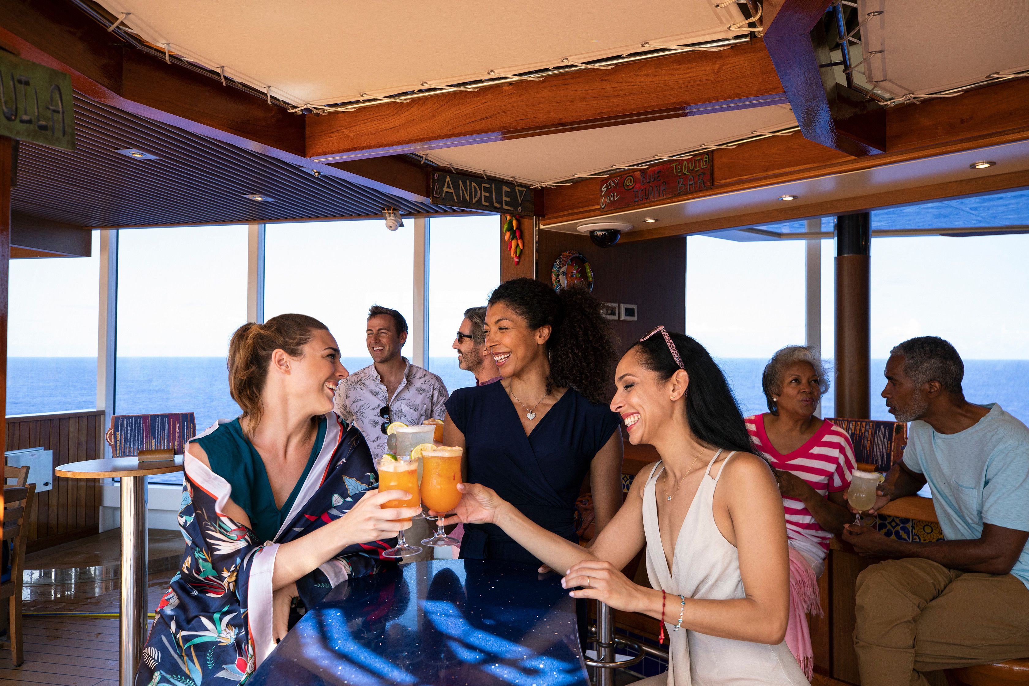 Guests enjoying tropical cocktails at BlueIguana Tequila Bar on Carnival cruise, with ocean views and lively conversation in a casual setting.