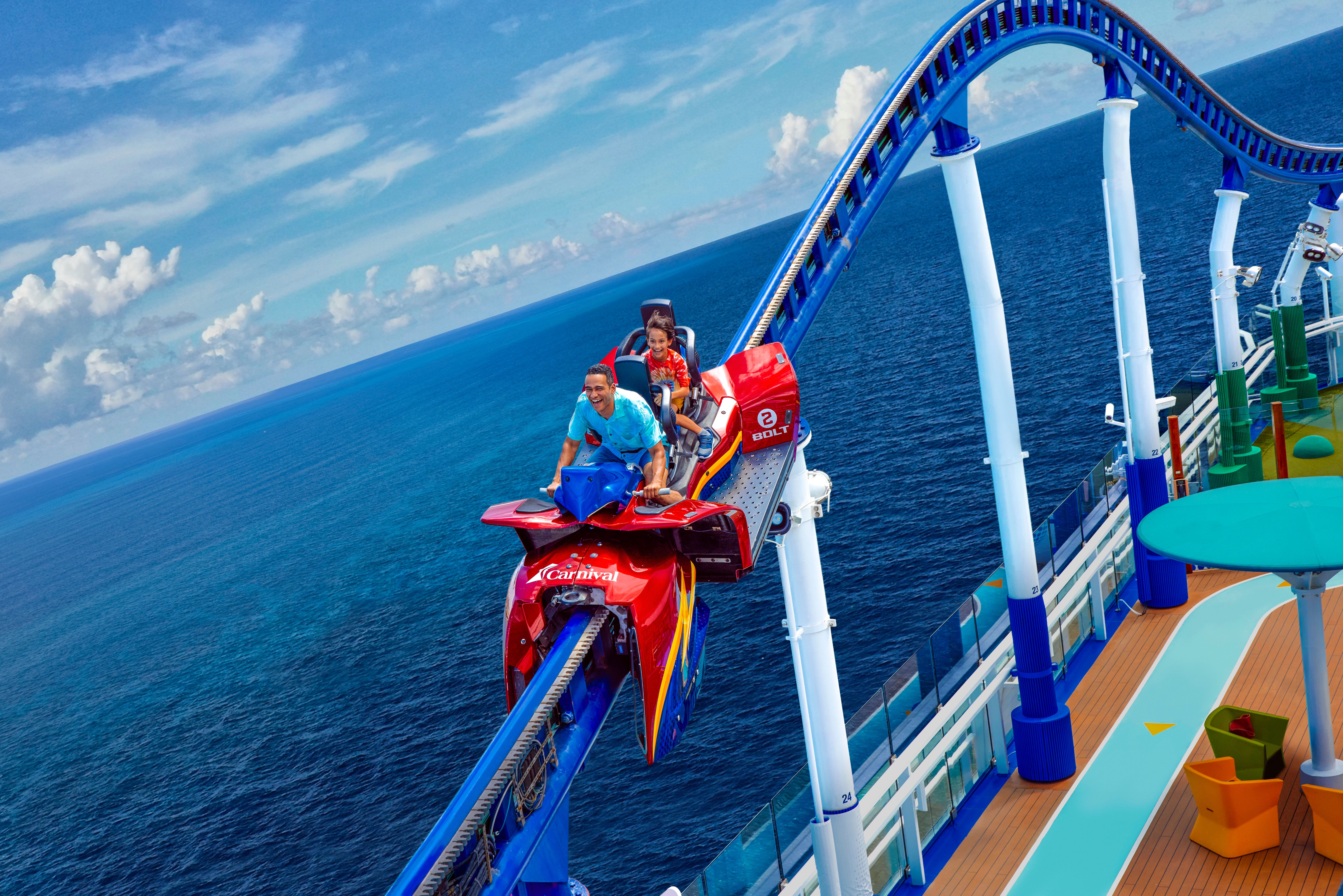 Guests ride BOLT roller coaster on Carnival cruise ship, soaring above ocean with thrilling views and open-air track.