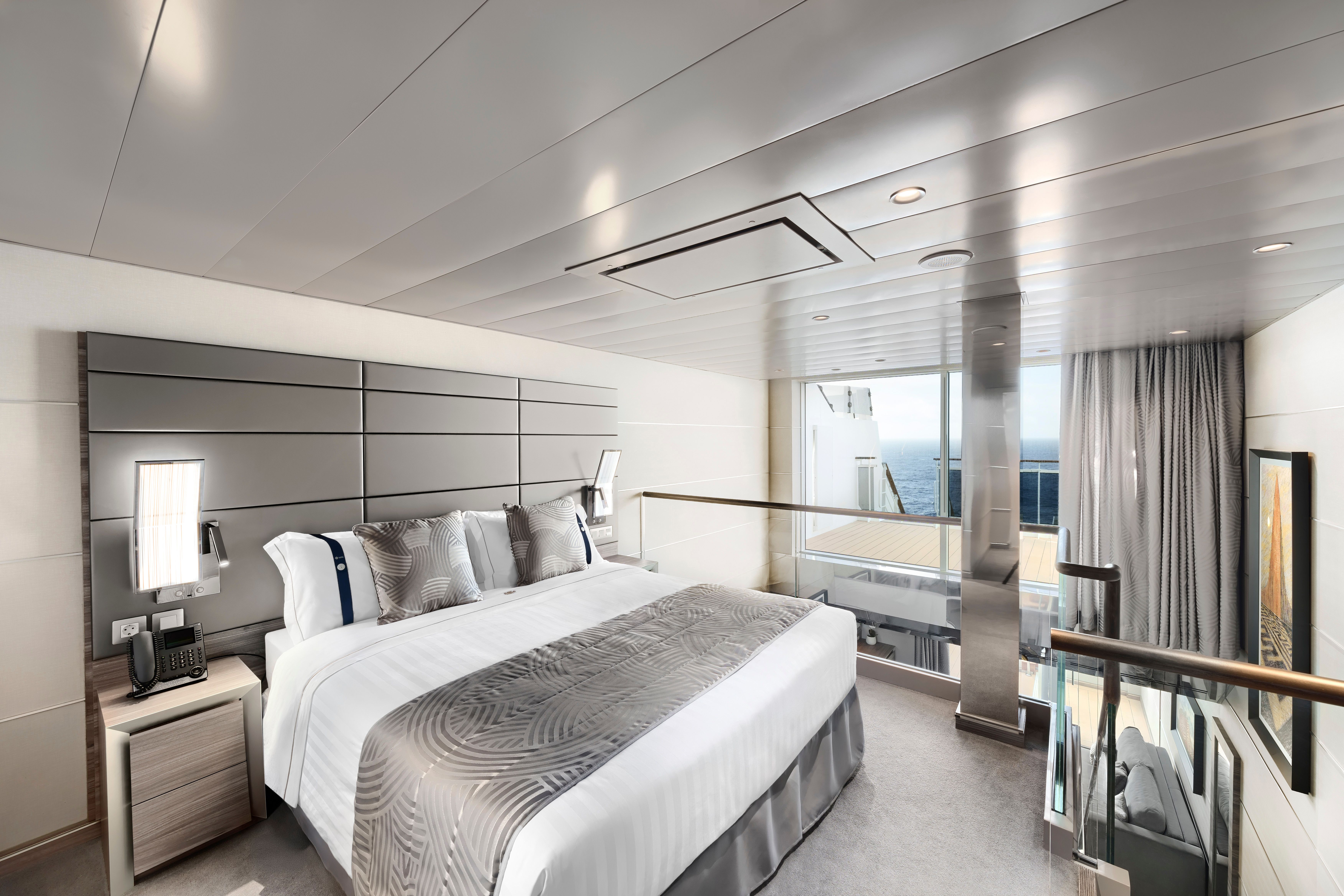 Luxurious MSC Yacht Club Duplex Suite featuring a king bed, modern décor, oceanview balcony, and glass-railed staircase to a private living area below.