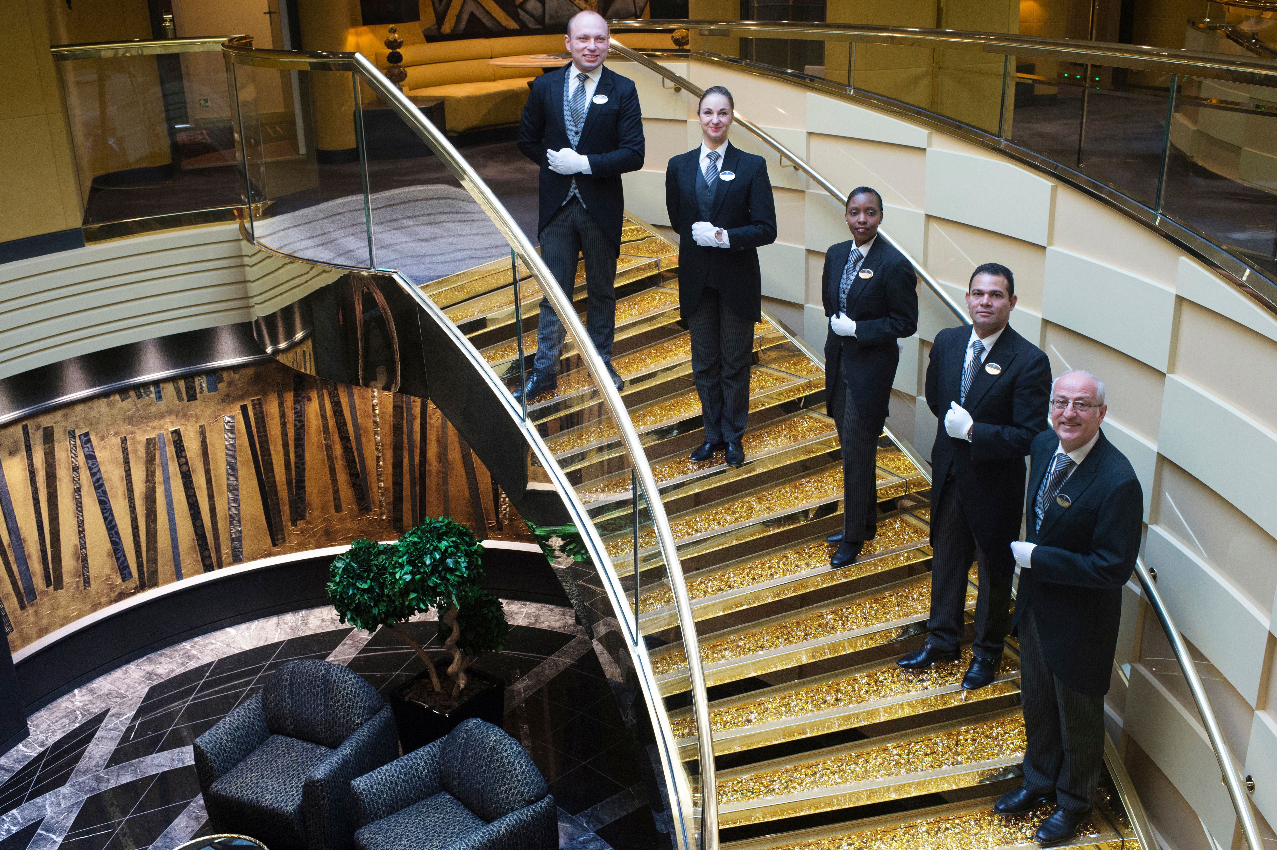 Elegant MSC Yacht Club butlers in formal attire pose on a Swarovski crystal staircase, showcasing luxury service and concierge excellence onboard.