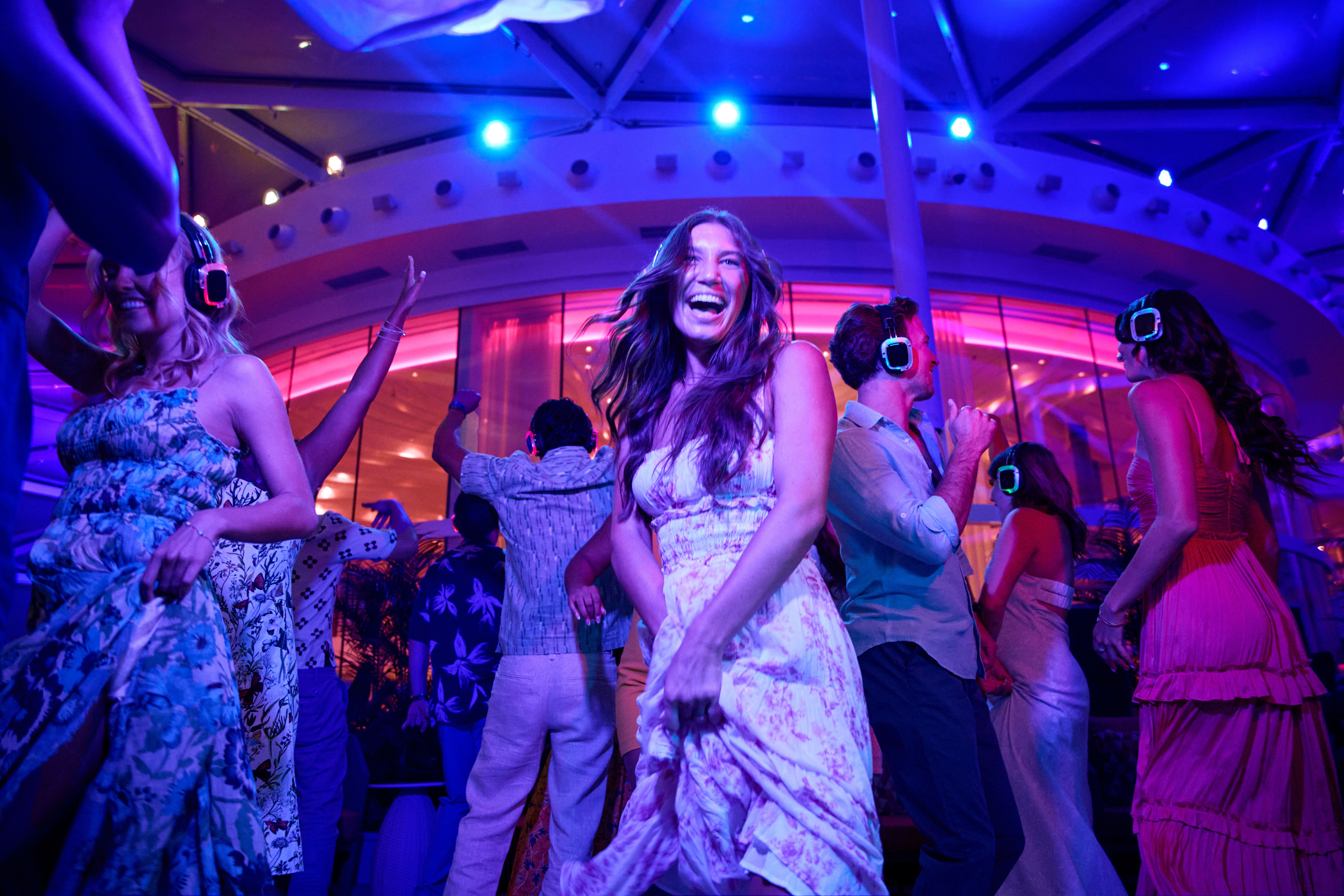 Guests dancing at a Royal Caribbean silent disco in the Solarium, wearing glowing headphones under vibrant purple and blue lights.
