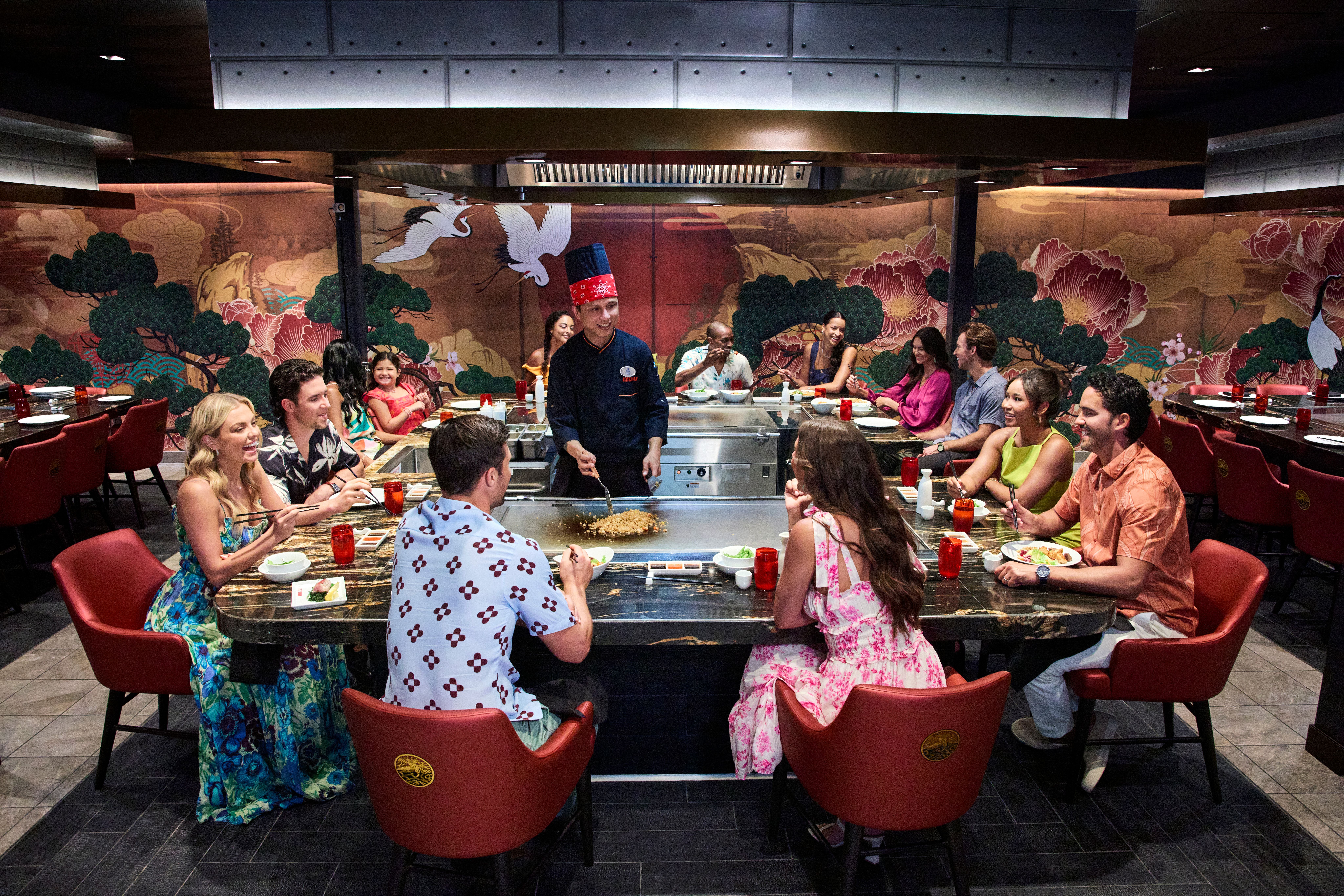 Groups enjoying dinner and live teppanyaki cooking at Izumi Hibachi on Royal Caribbean, as a chef performs at the grill table.