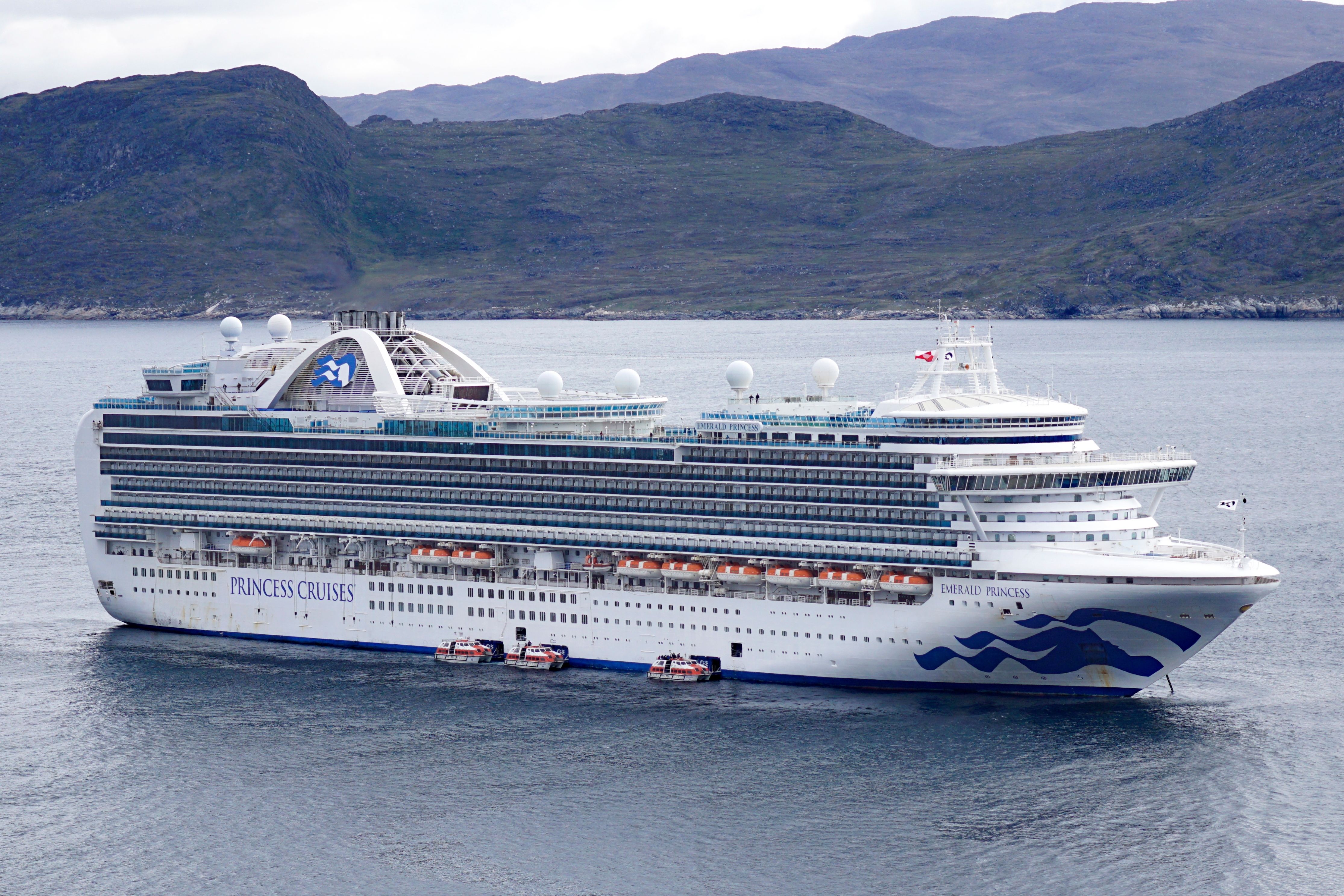Princess Cruises’ Emerald Princess sailing near a rugged coastline, showcasing its elegant multi-deck exterior and signature sea-blue hull design.