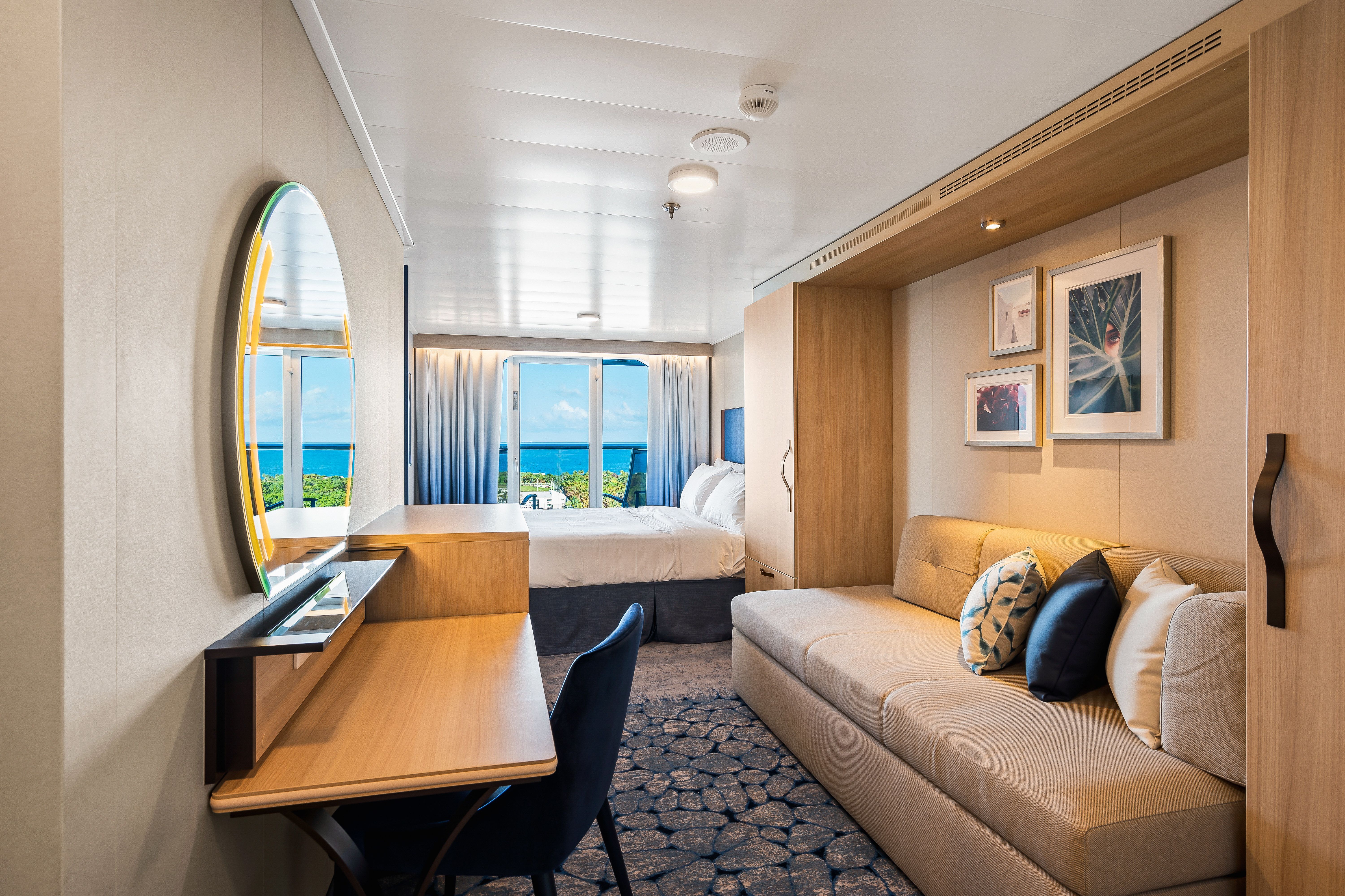 Modern connecting oceanview balcony stateroom with sitting area, vanity desk, and large window overlooking the sea on Royal Caribbean.