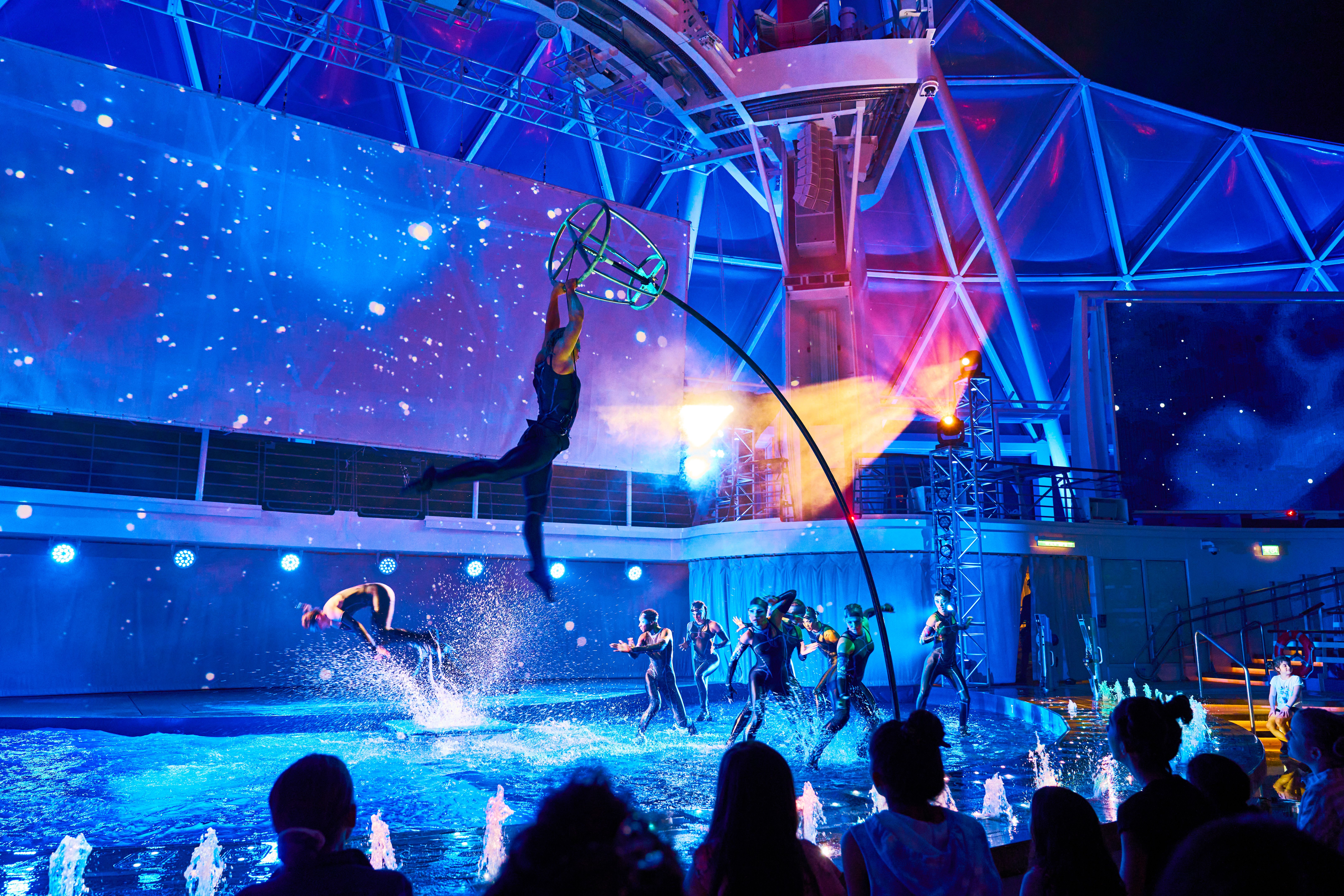AquaTheater night show on Royal Caribbean with acrobats, water stunts, and vibrant lighting thrilling a live audience.