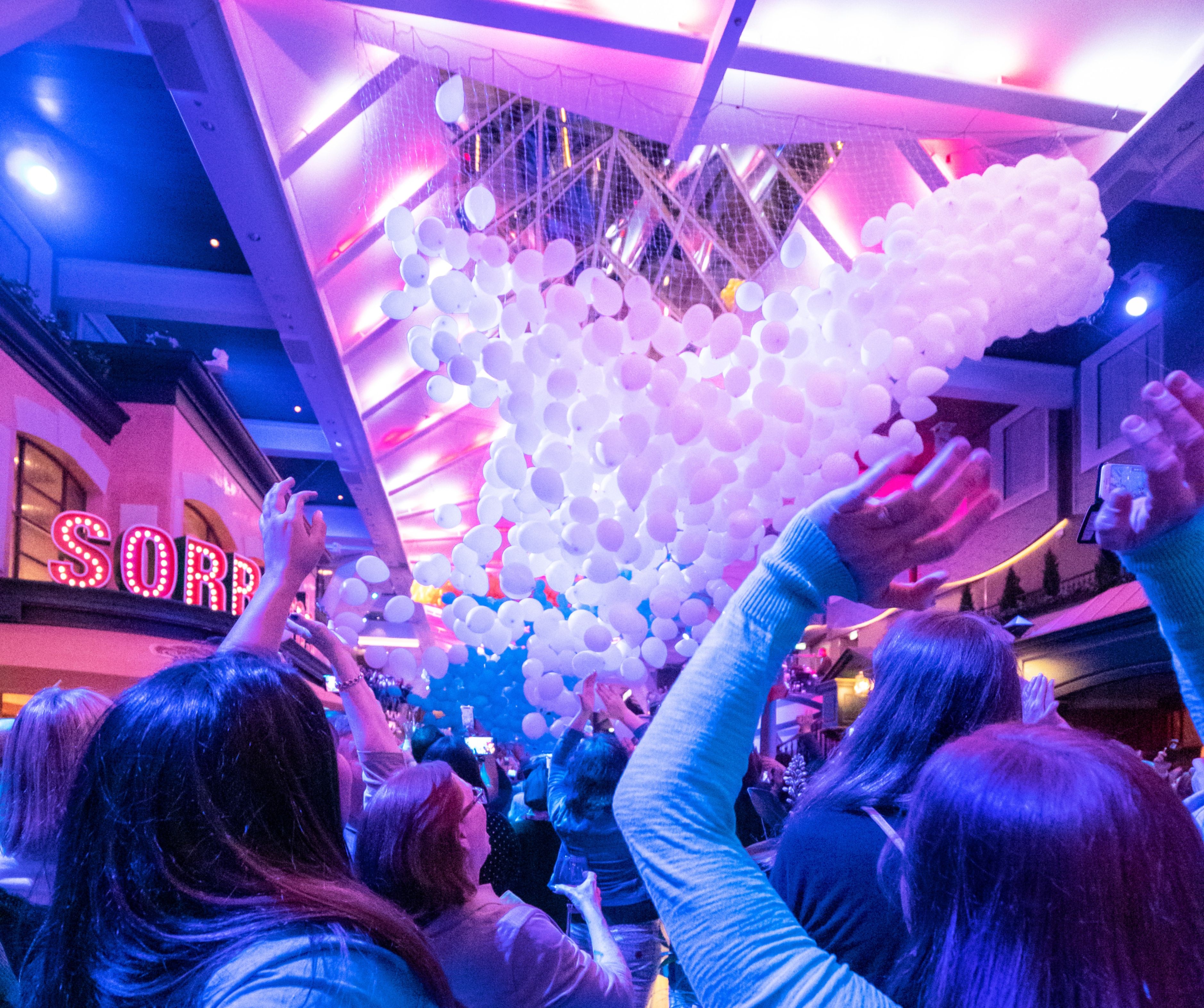 Cruise guests gather under a balloon net at Royal Caribbean’s Royal Promenade during a vibrant indoor party celebration.
