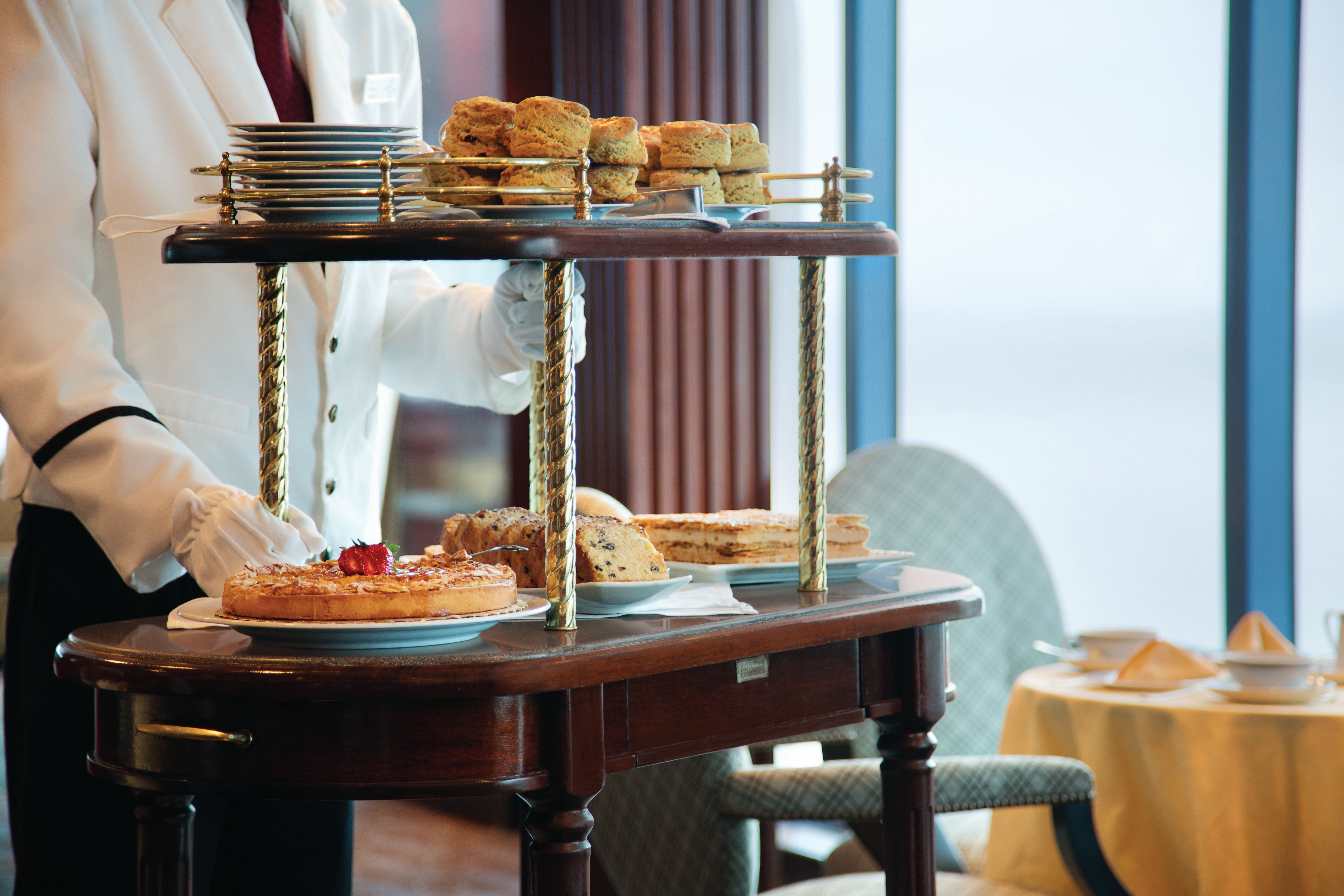 Afternoon tea service in Horizons Lounge on Oceania Riviera cruise, featuring a refined tea cart with pastries, scones, and elegant oceanview seating.