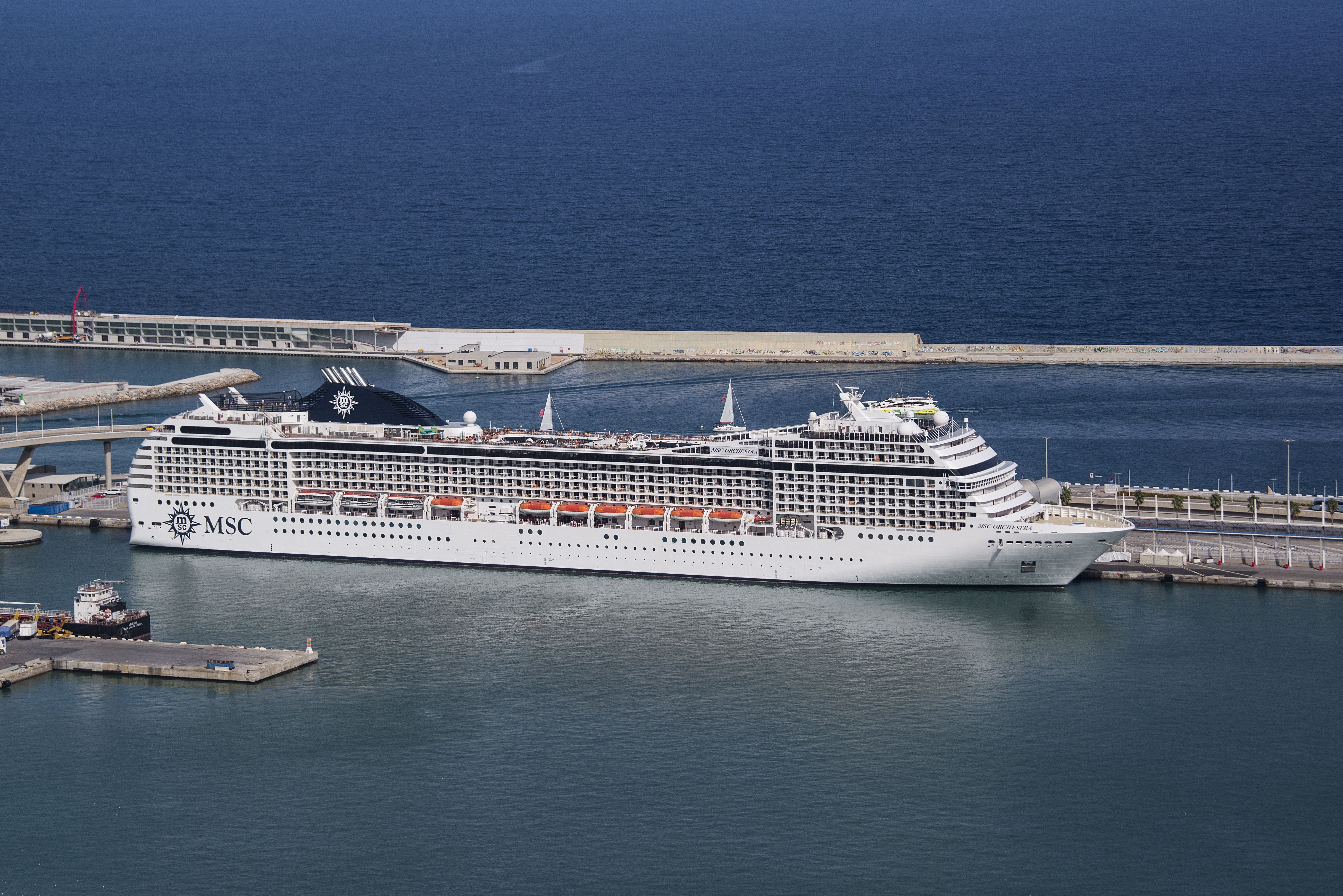 MSC cruise ship docked at the Barcelona cruise terminal with clear blue waters and modern port infrastructure in view.