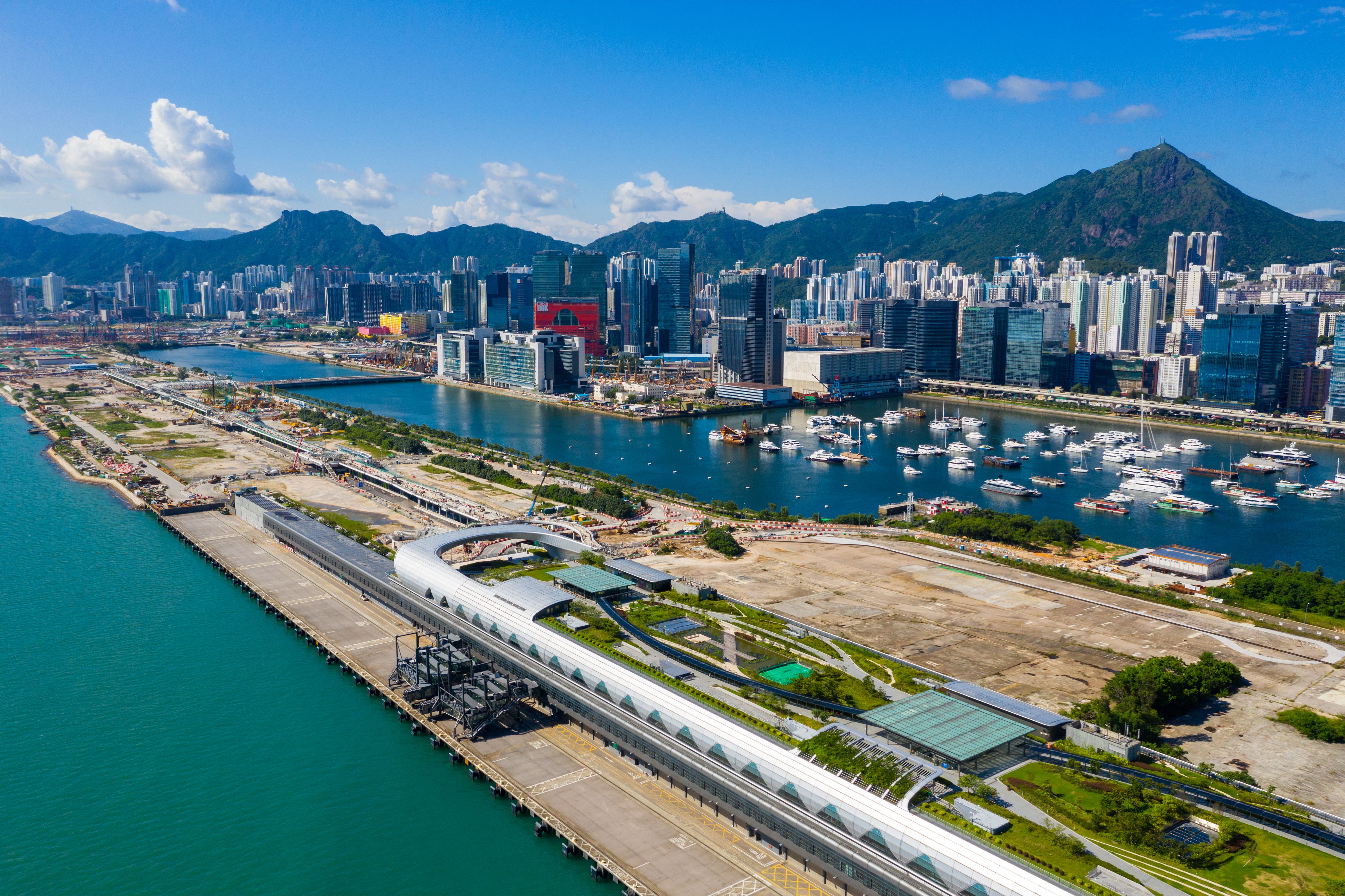 Kai Tak Cruise Terminal in Hong Kong with modern terminal design, Victoria Harbour views, and Kowloon skyline set against lush mountain backdrop.