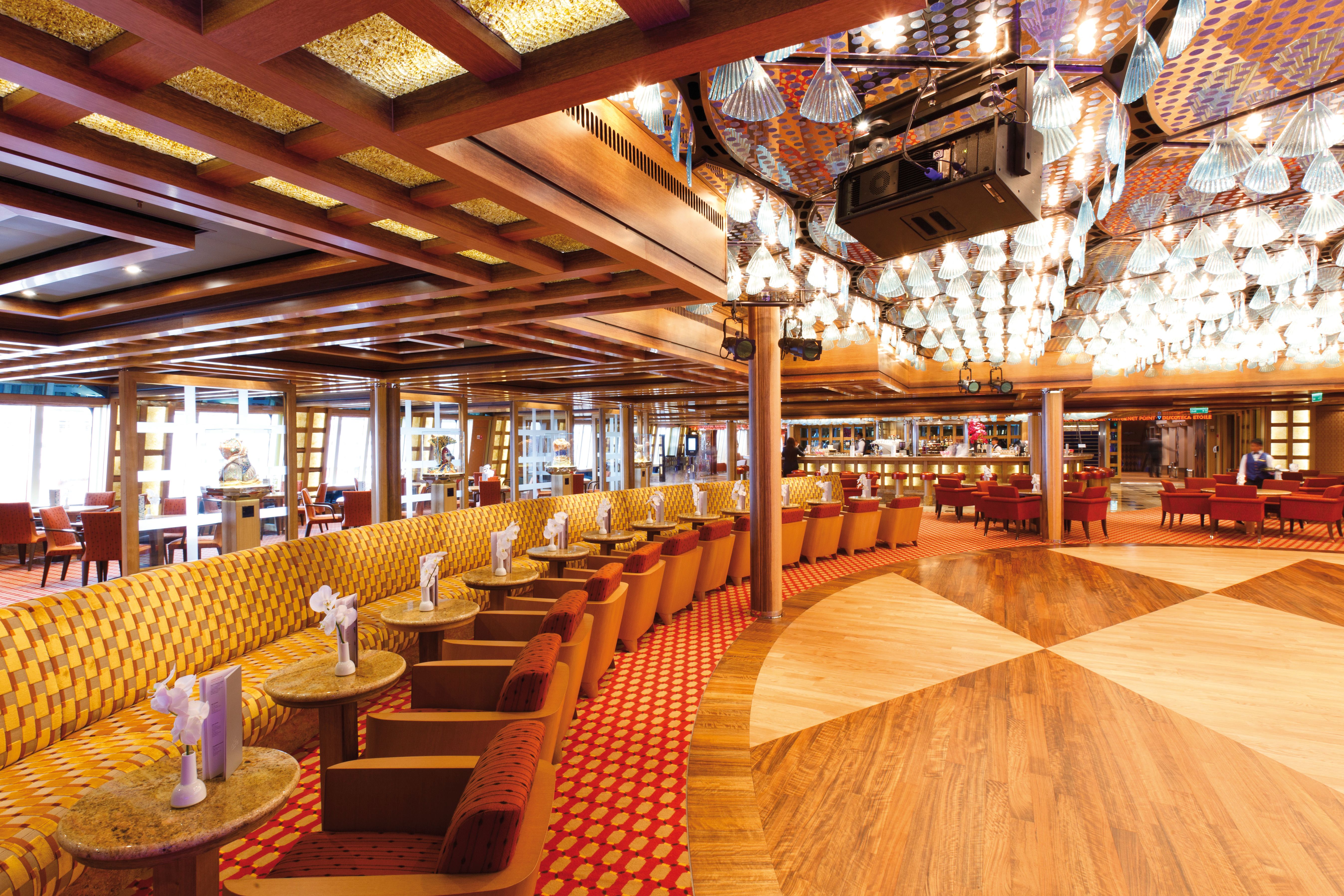 Elegant interior of Grand Bar Palatino on a cruise ship, featuring plush seating, a polished wood dance floor, and ornate ceiling lighting.
