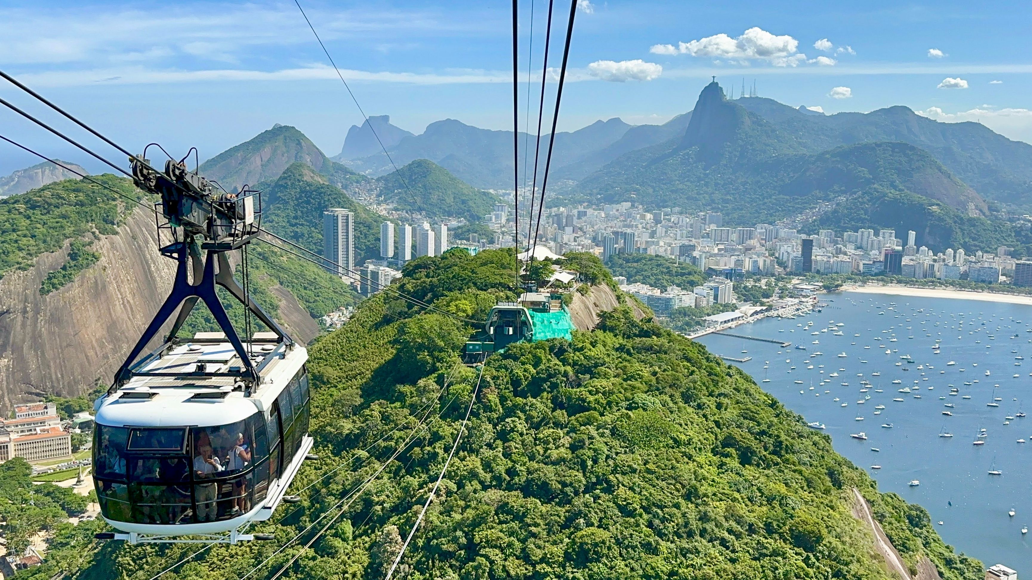 Sugarloaf Mountain cable car in Rio de Janeiro gliding above lush hills with city skyline, Copacabana Beach, and Christ the Redeemer in the distance.