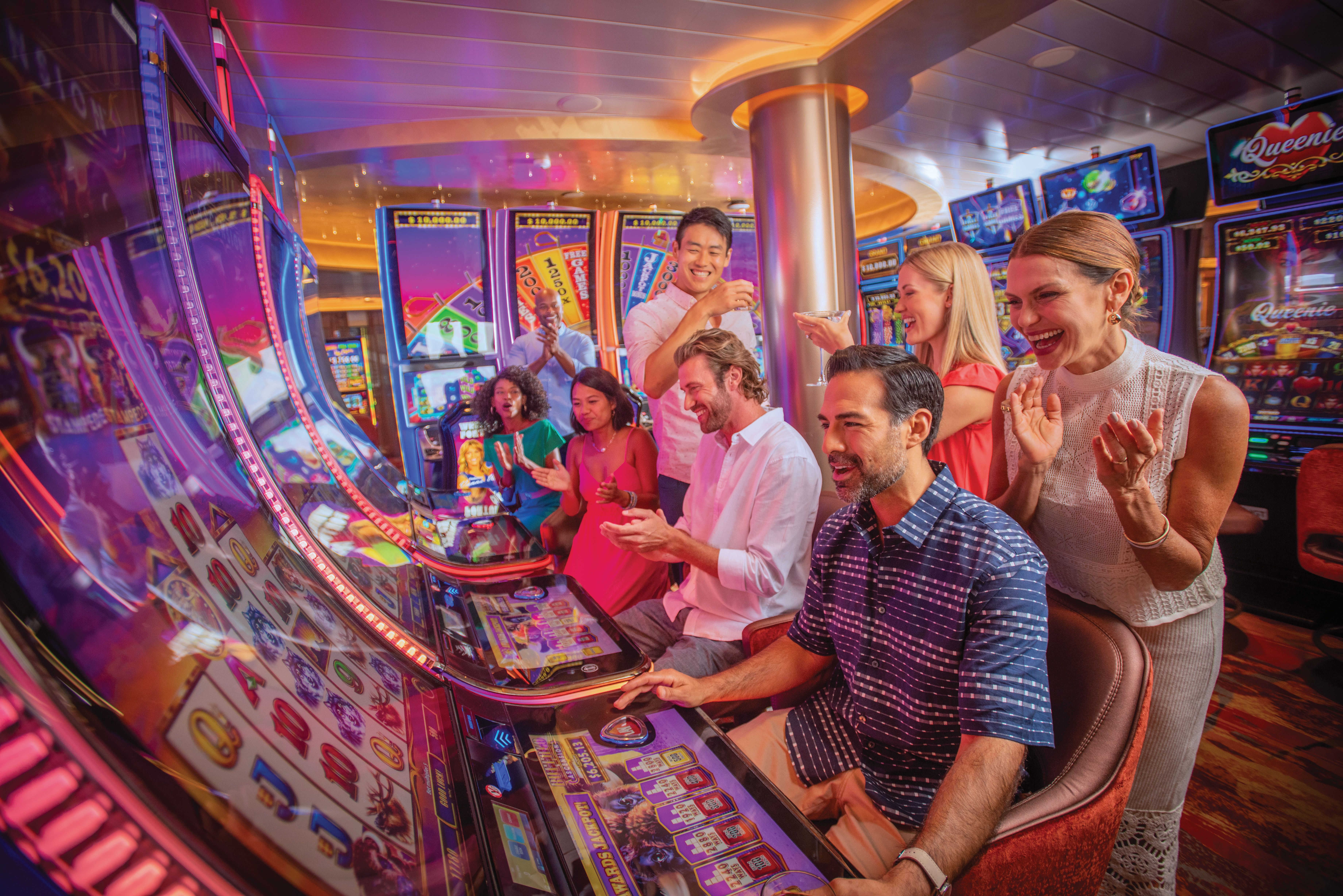 Group of guests enjoying slot machines at Carnival cruise ship casino, surrounded by vibrant lights, colorful screens, and celebratory atmosphere.