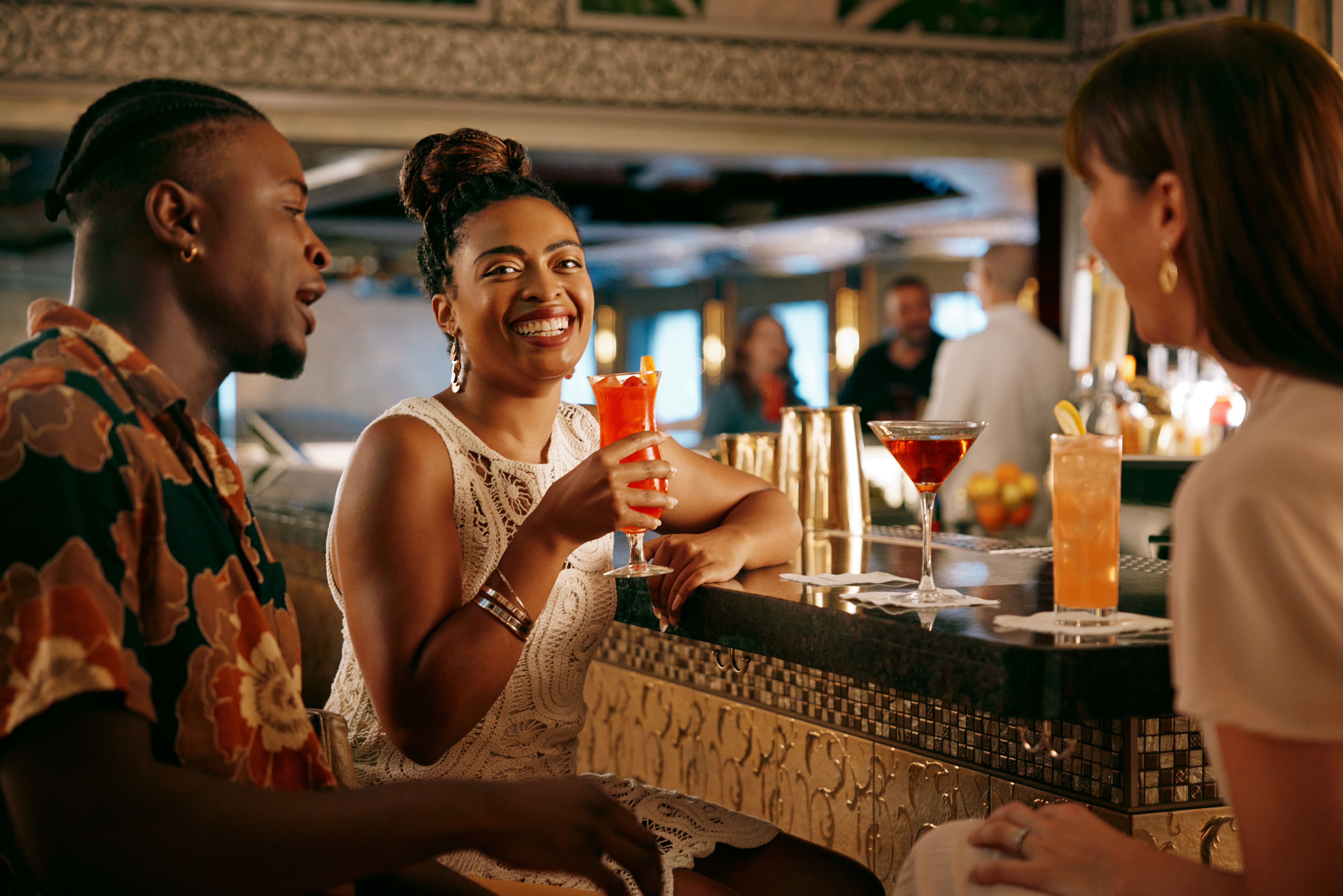 Guests enjoying colorful cocktails at a Carnival cruise ship bar, with lively conversation and elegant décor creating a vibrant onboard nightlife scene.