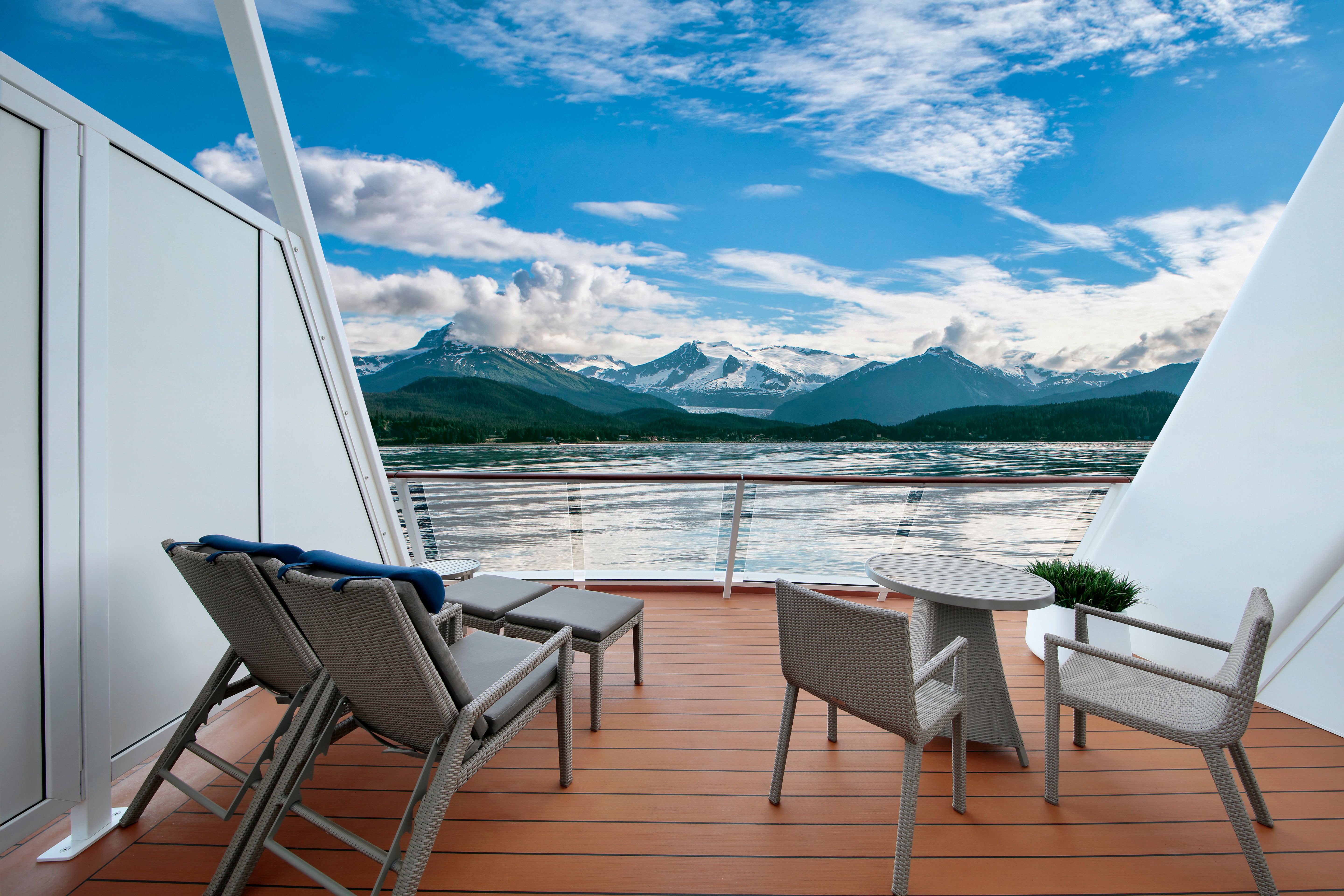 Spacious cruise balcony with lounge seating and stunning sea views of Alaska’s snow-capped mountains and serene coastal waters.