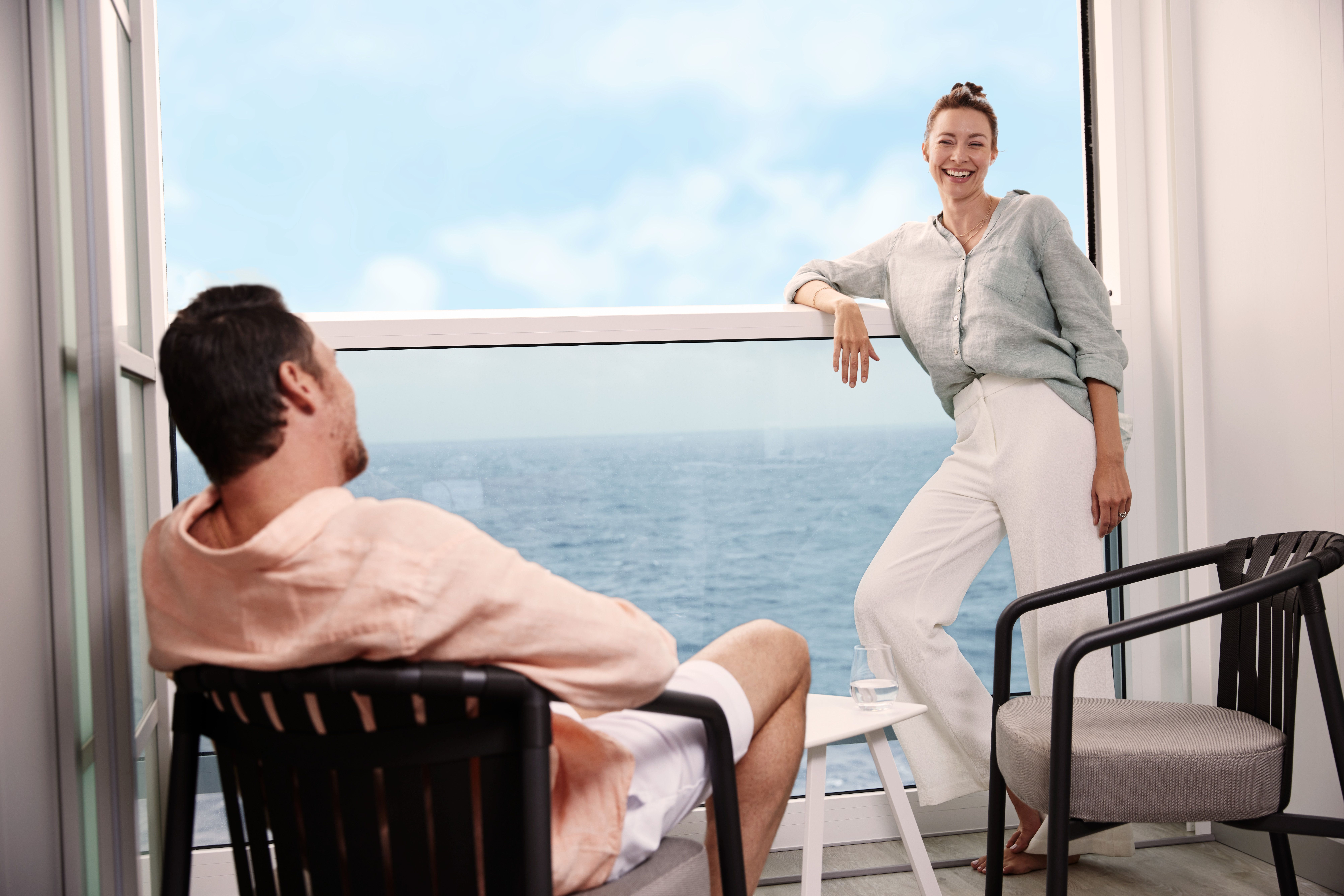 Couple relaxing on the Infinite Veranda of a Celebrity Cruises stateroom, enjoying ocean views through floor-to-ceiling glass.