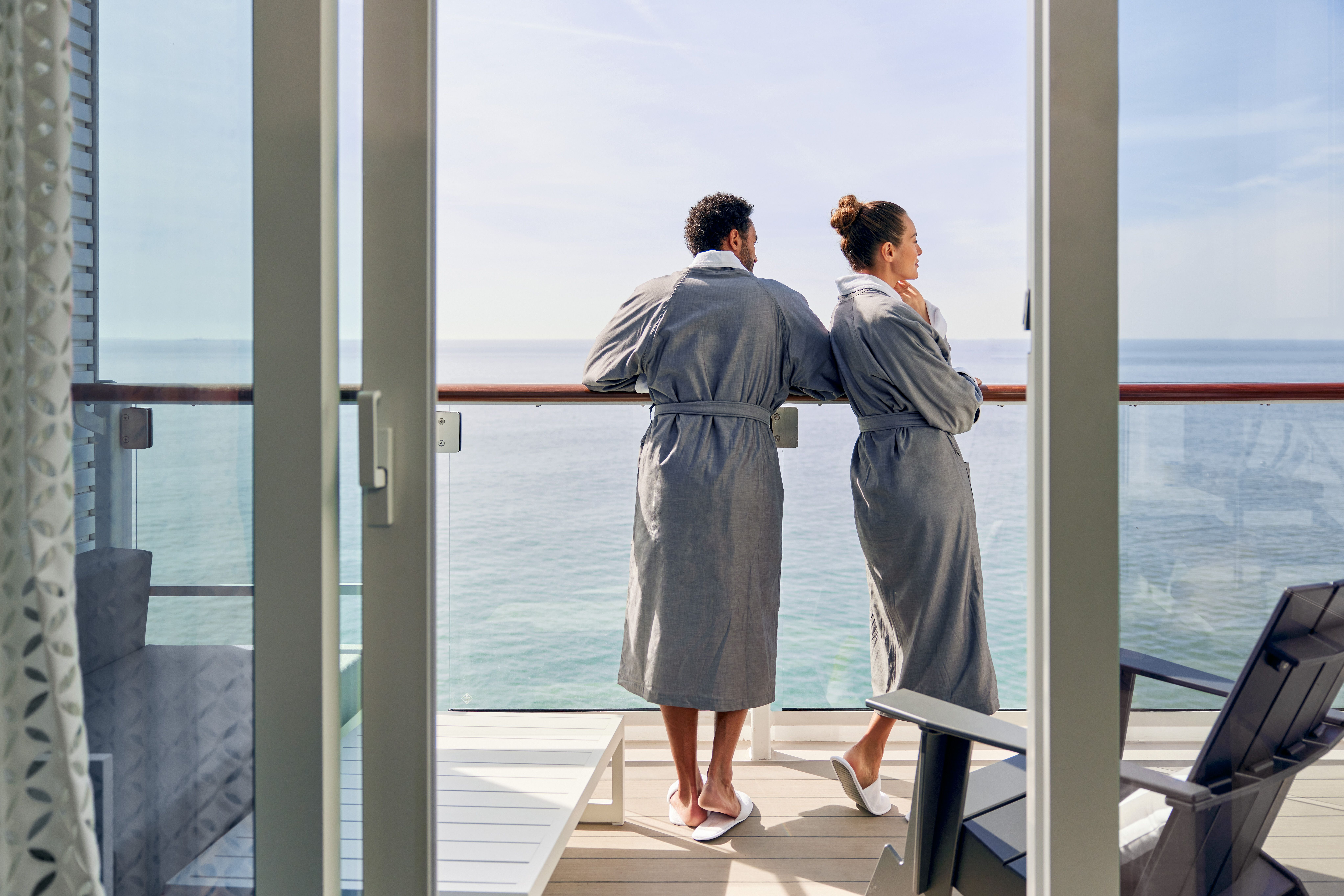 Couple in robes enjoying a peaceful morning on a cruise ship balcony with ocean views and serene ambiance.