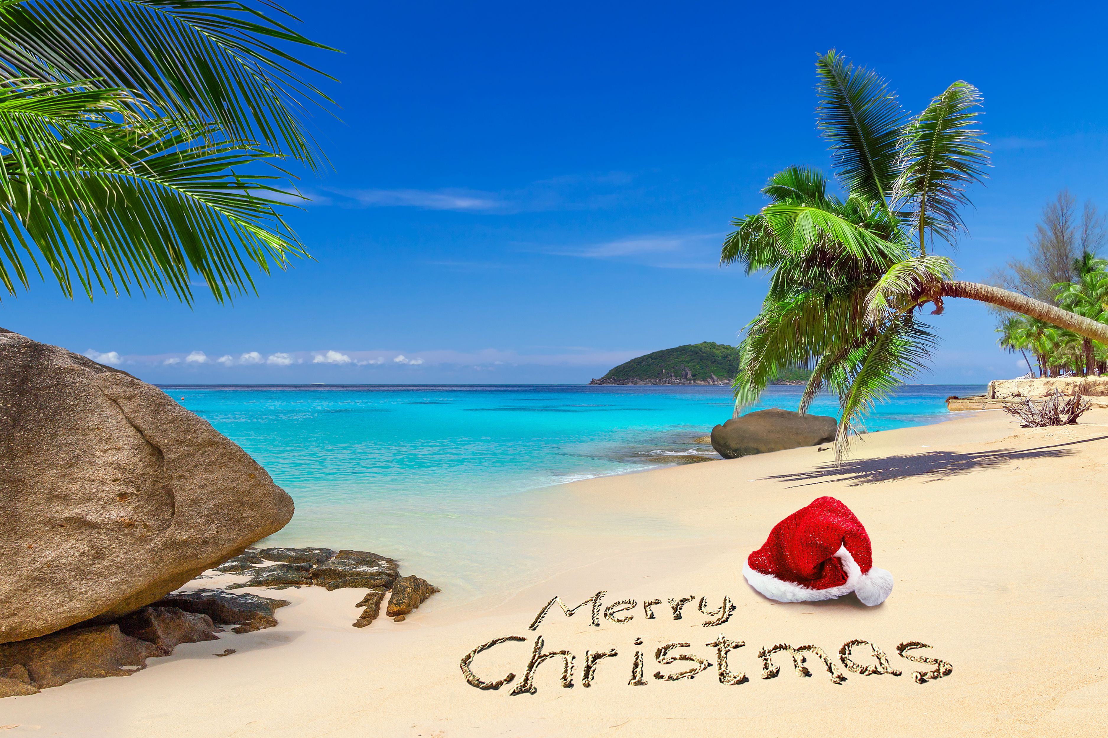 Tropical beach with turquoise waters and palm trees, featuring "Merry Christmas" written in the sand and a Santa hat for a festive Caribbean holiday cruise vibe.