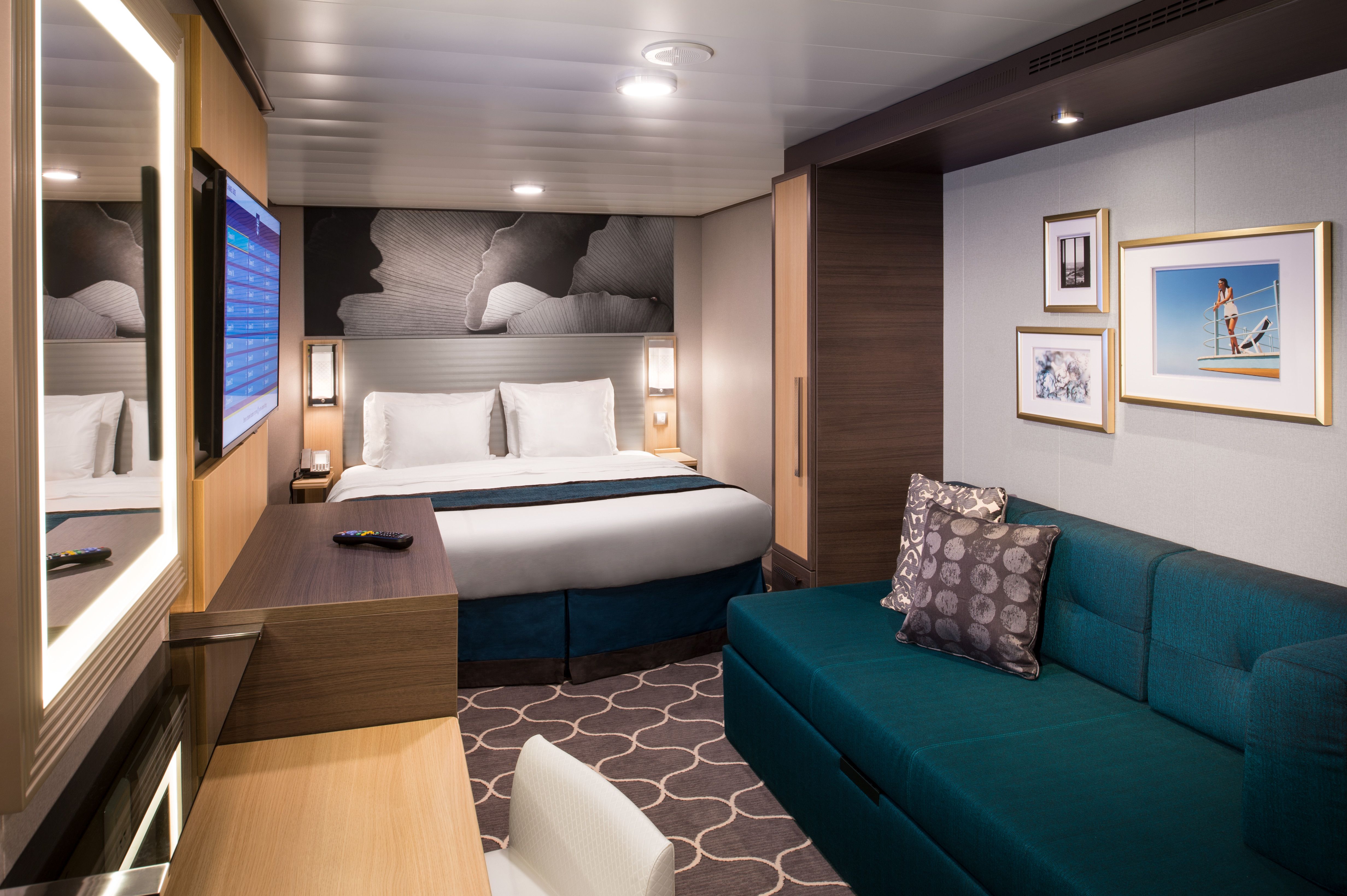 Modern Interior stateroom featuring a king bed, sofa, desk, and wall-mounted TV — ideal for relaxation after a day at sea.