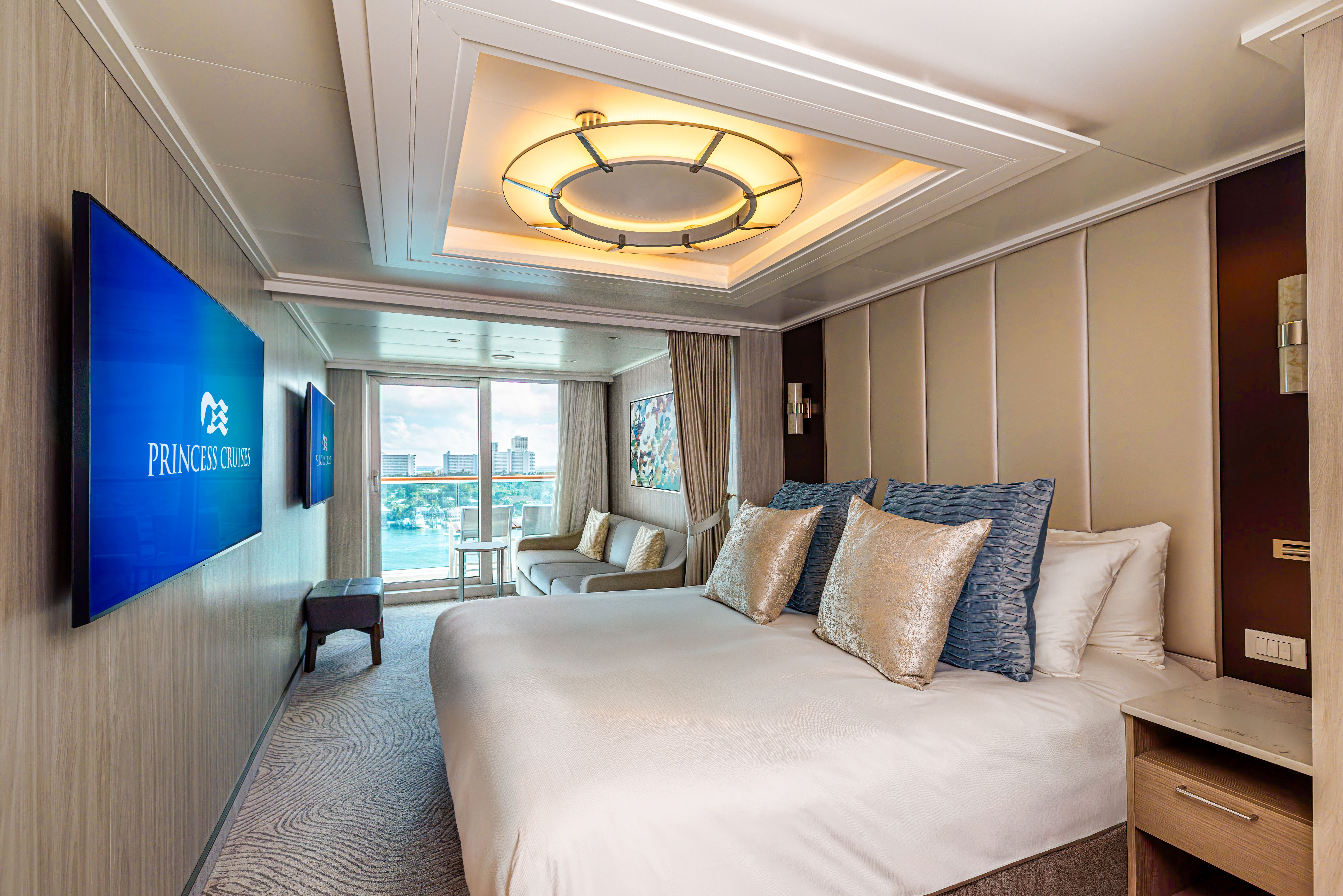 Sanctuary Mini-Suite bedroom with king bed, plush pillows, modern lighting and large flat-screen TV in a stylish Princess Cruises stateroom.
