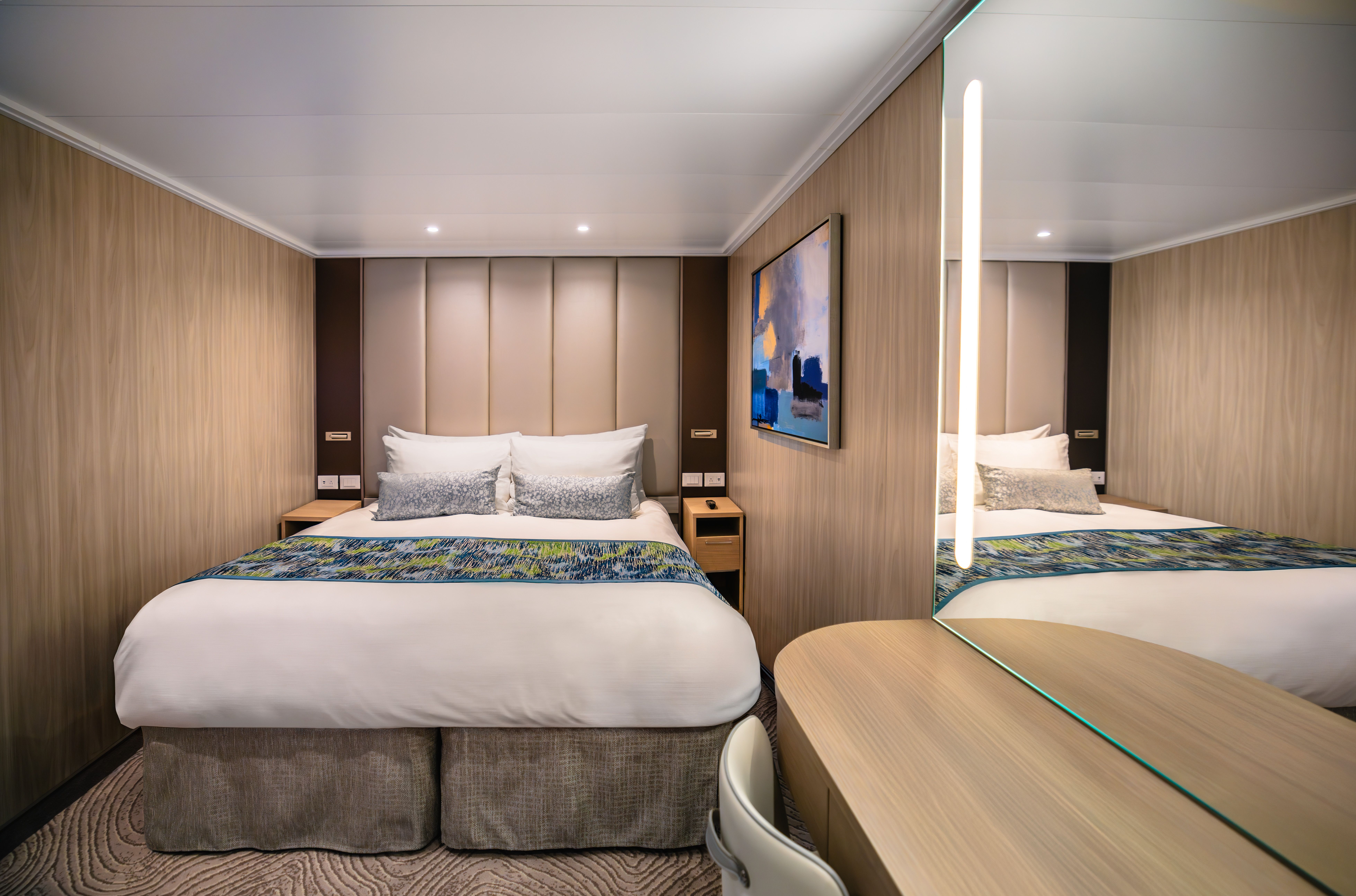 Interior stateroom with queen bed, plush bedding, wood-paneled walls and modern vanity desk on a Princess Cruises ship.