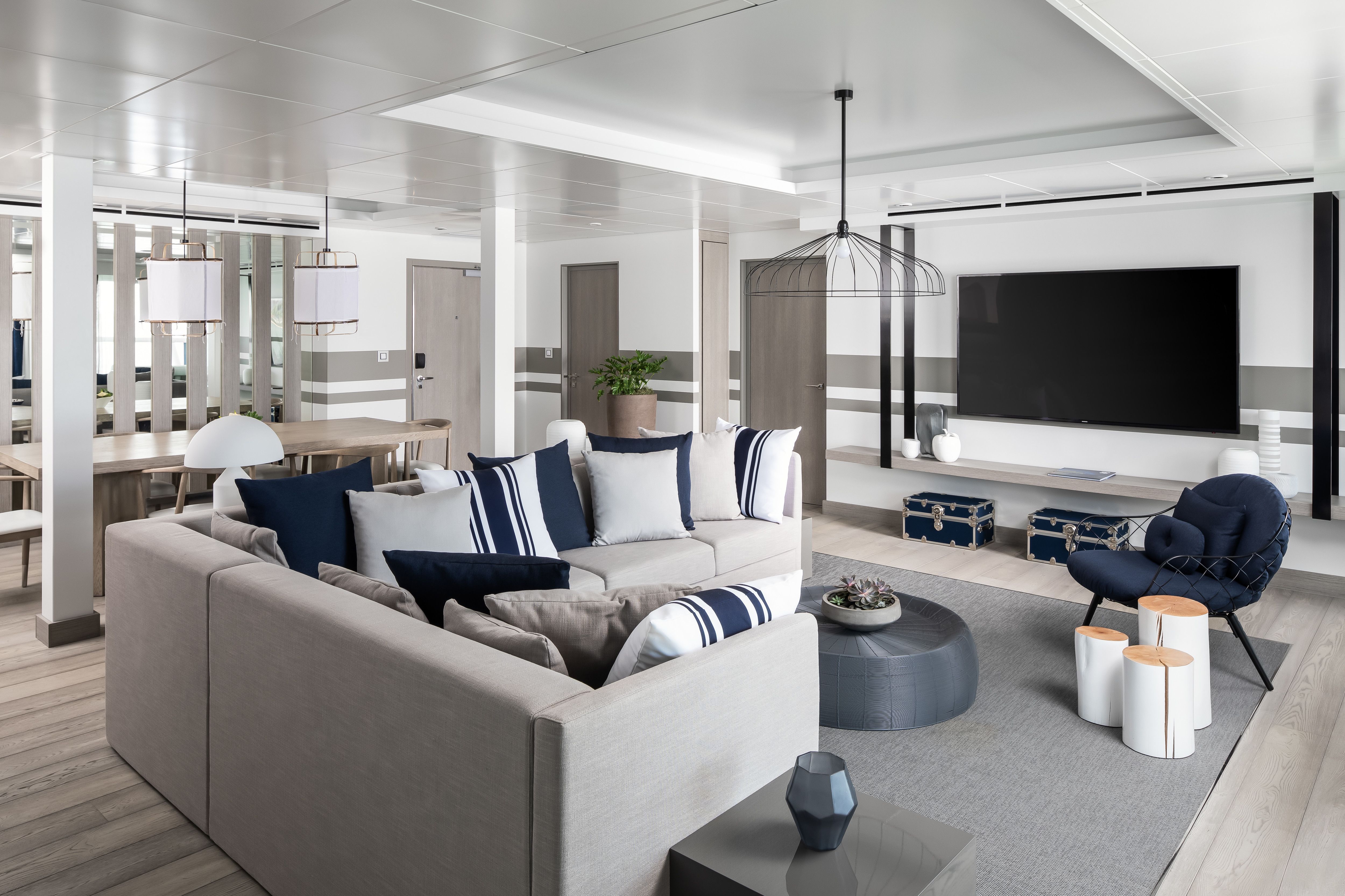 Celebrity Xcel Penthouse Suite living room with modern sectional sofa, navy accent pillows, large flat-screen TV and open dining area