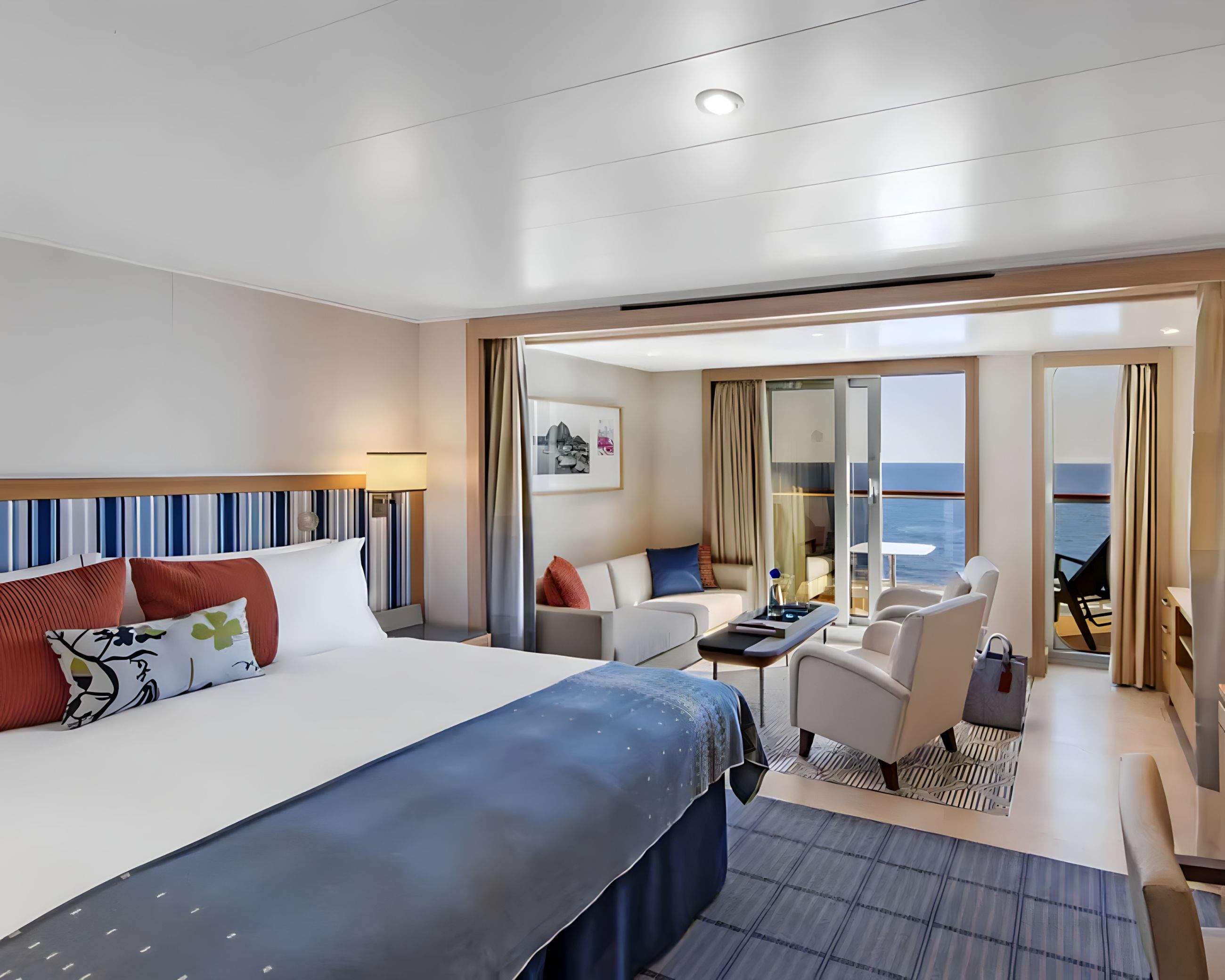 Penthouse Junior Suite with king-size bed, separate sitting area and private balcony, offering ocean views and contemporary Scandinavian design on a luxury cruise ship.
