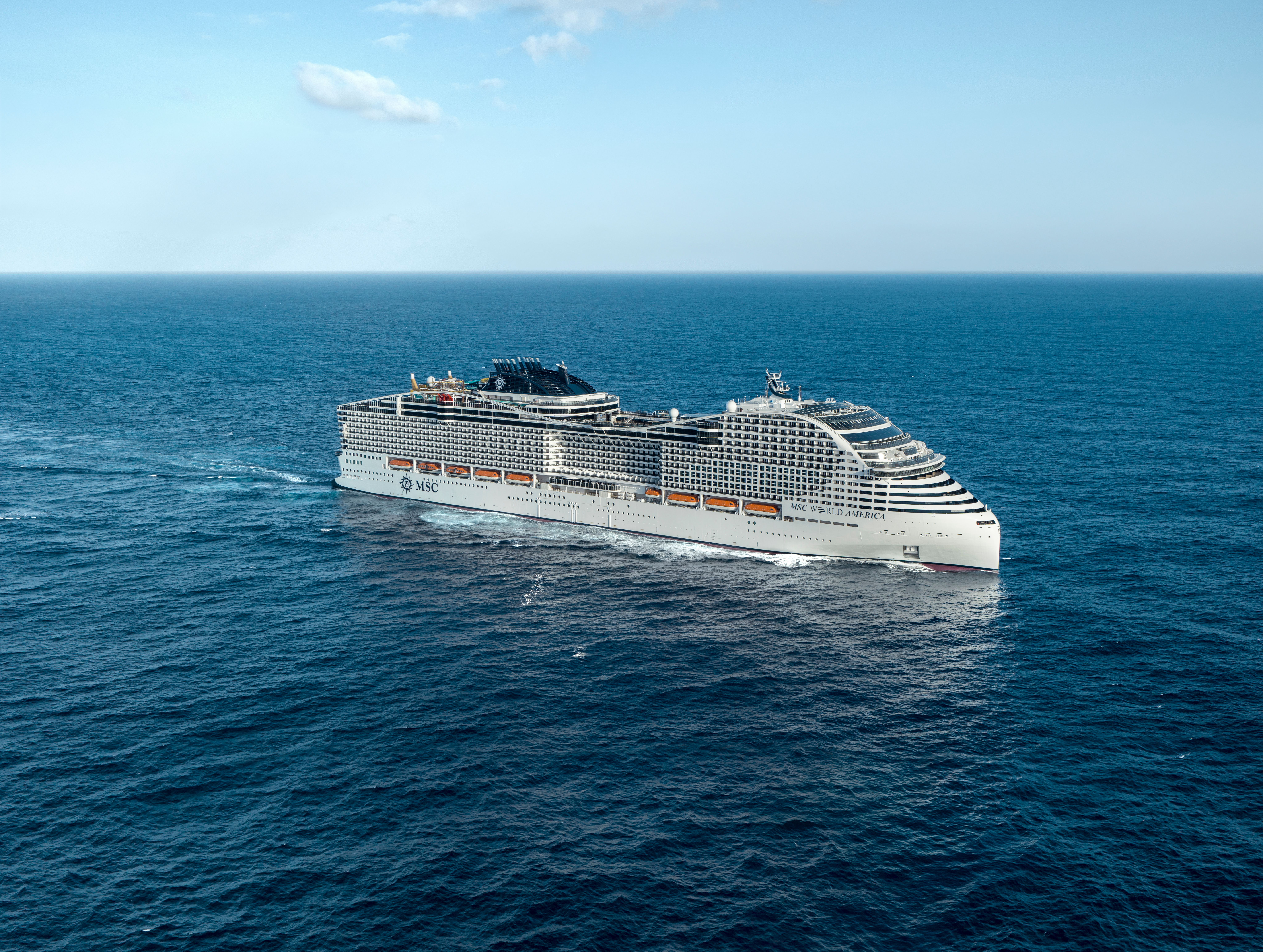 MSC World America cruise ship aerial view sailing in open ocean, luxury MSC Cruises vessel with expansive decks and balconies under clear blue sky