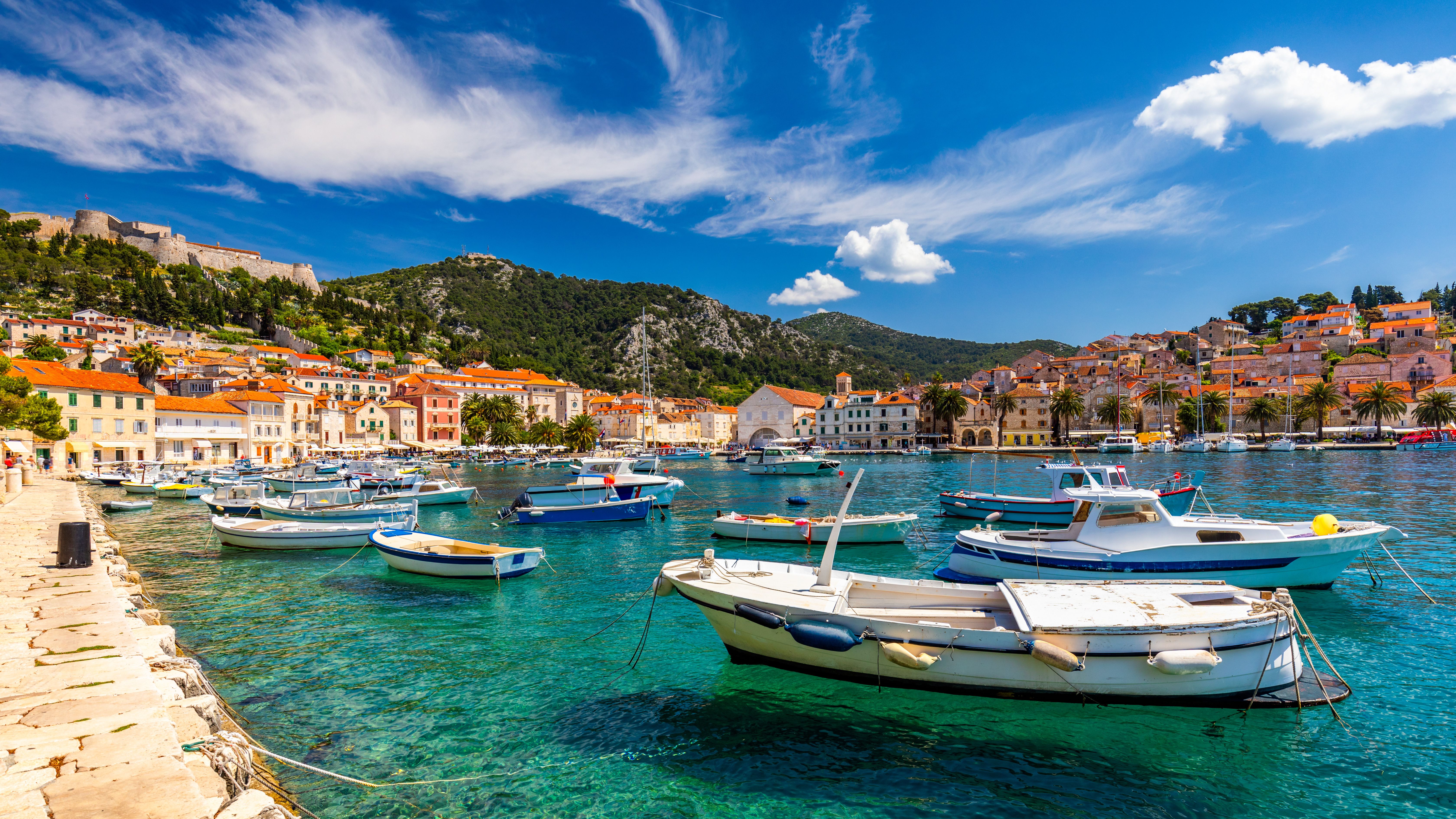 Hvar harbor with small boats on turquoise Adriatic water, historic stone town and hillside fortress, scenic Croatia island day trip from Dubrovnik cruise excursion