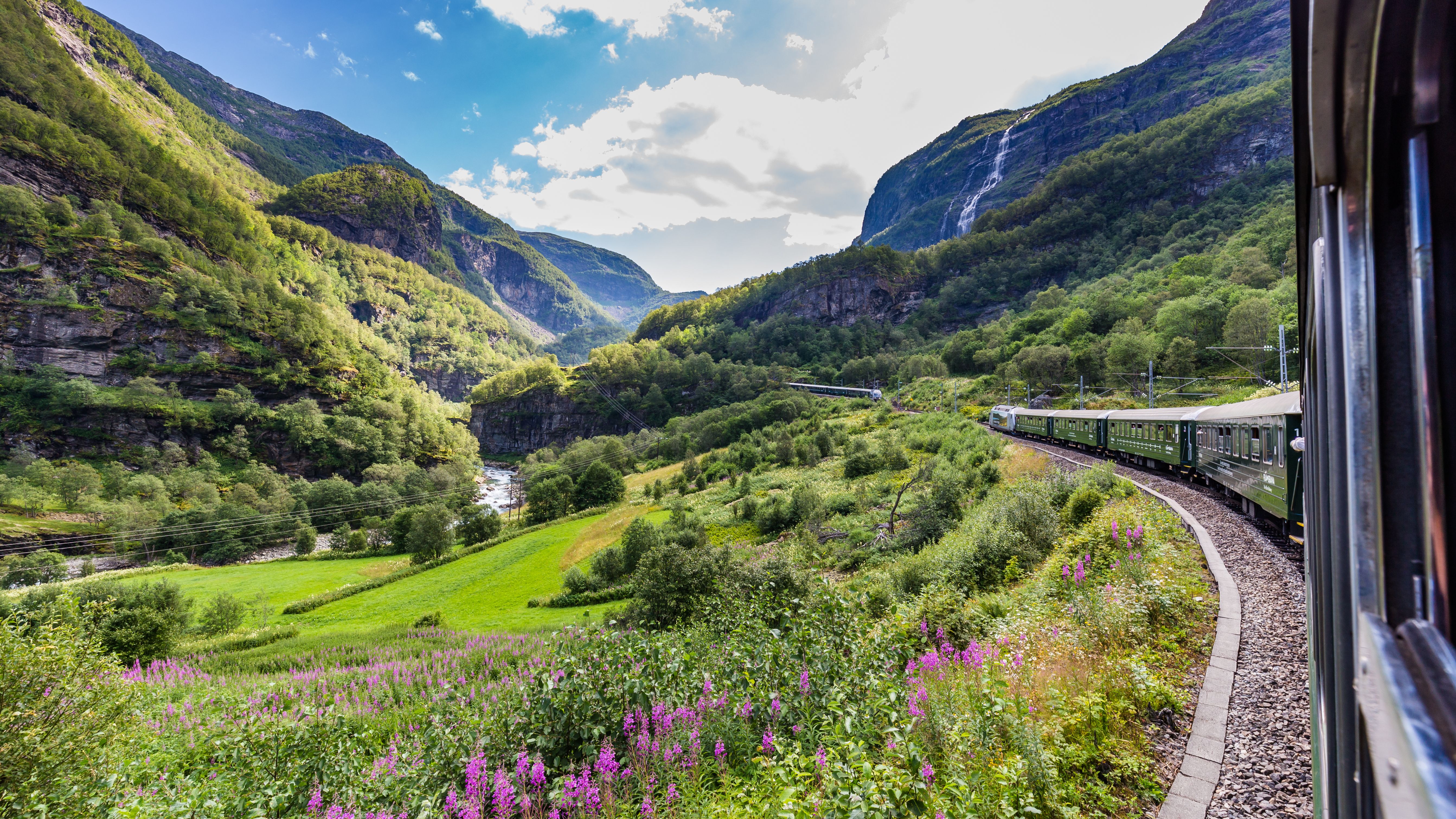 Flam Railway scenic train through Norway fjords, lush green valley, waterfalls and mountains—popular cruise shore excursion in Flam with panoramic views and winding tracks