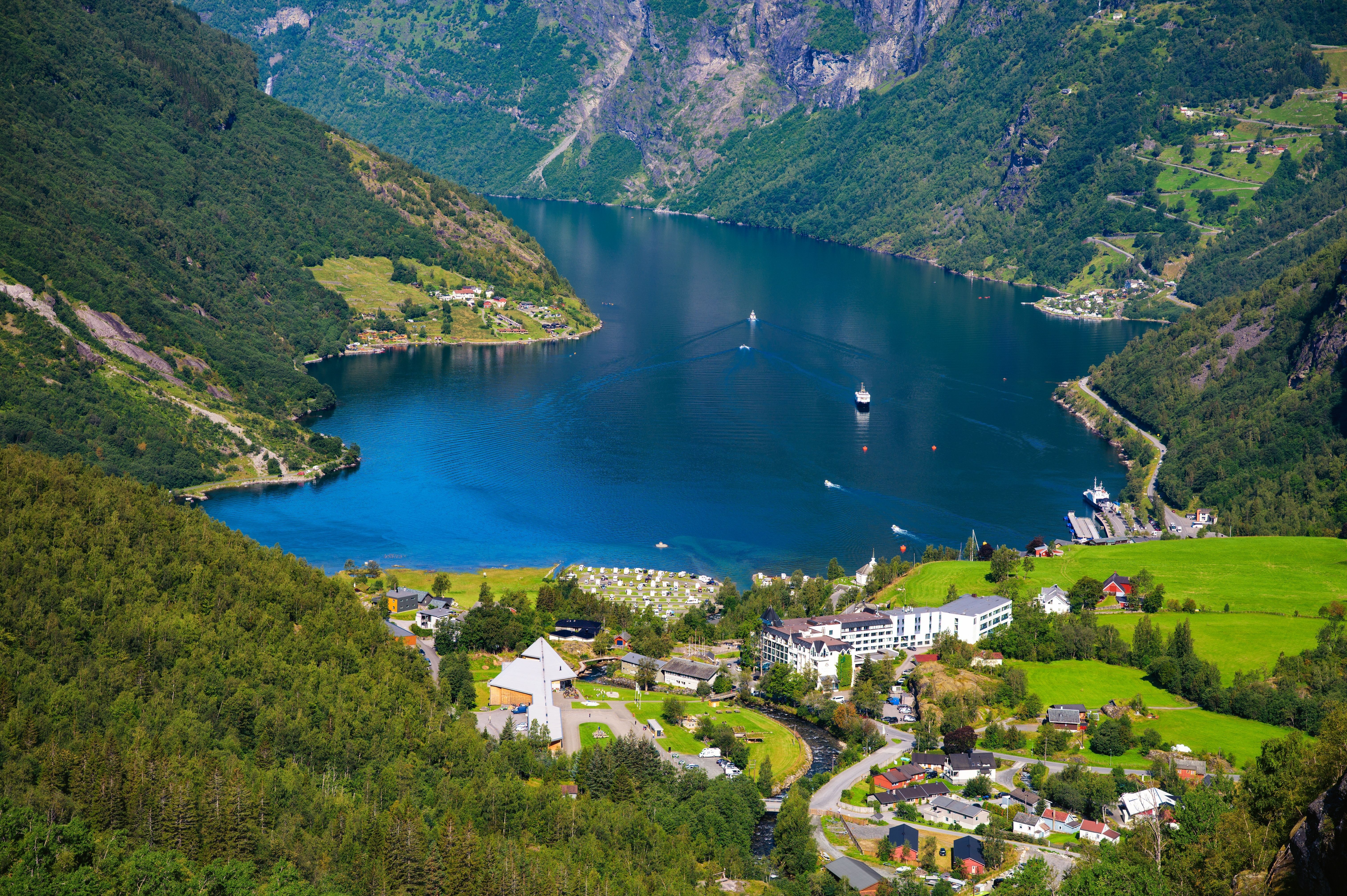 Aerial view of Geirangerfjord Norway with cruise ships and boats, steep green mountains, village and waterfront—iconic fjord cruise destination and shore excursion scenery