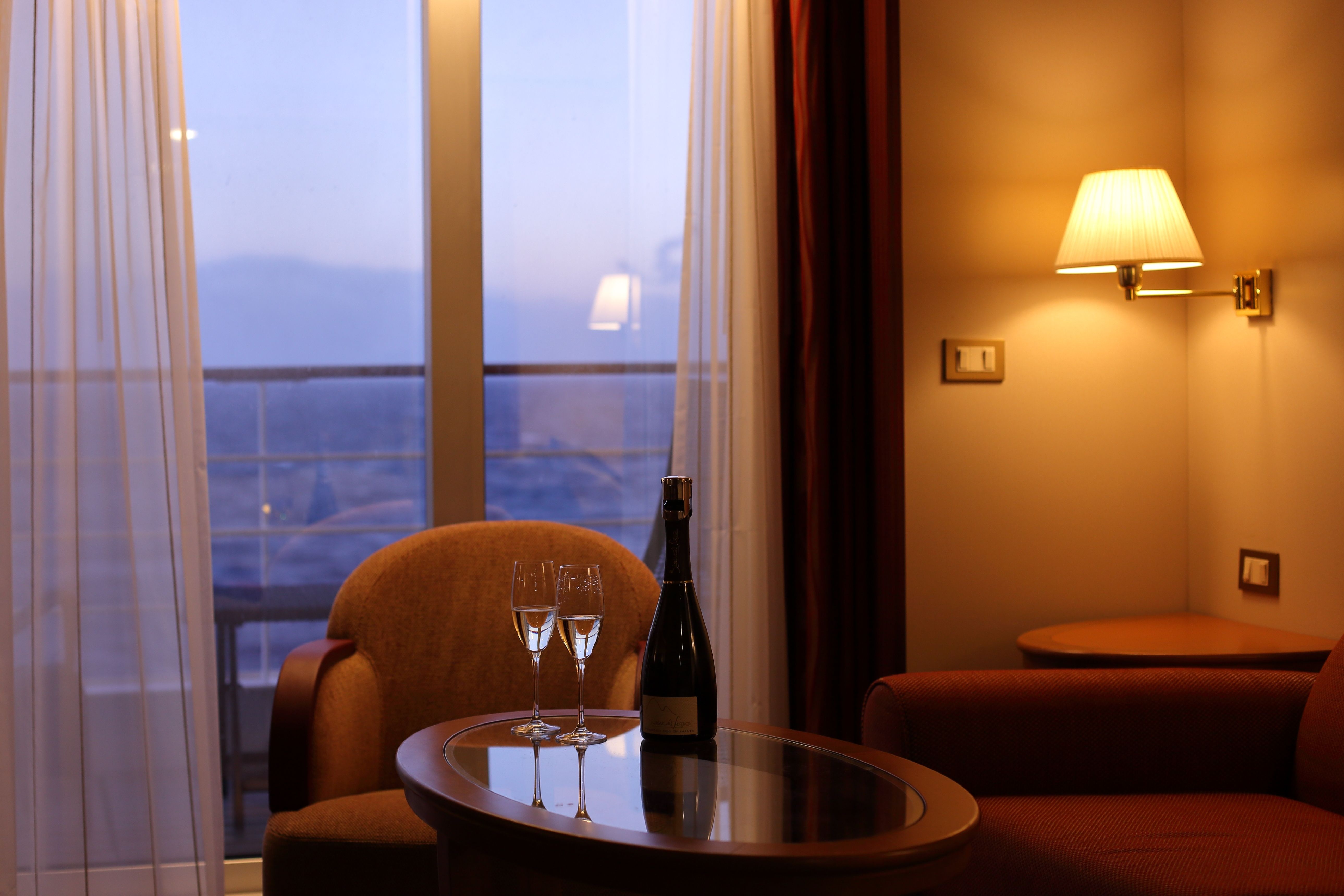 Luxury river cruise suite with champagne, cozy lounge seating, and private balcony overlooking scenic river views at sunset.