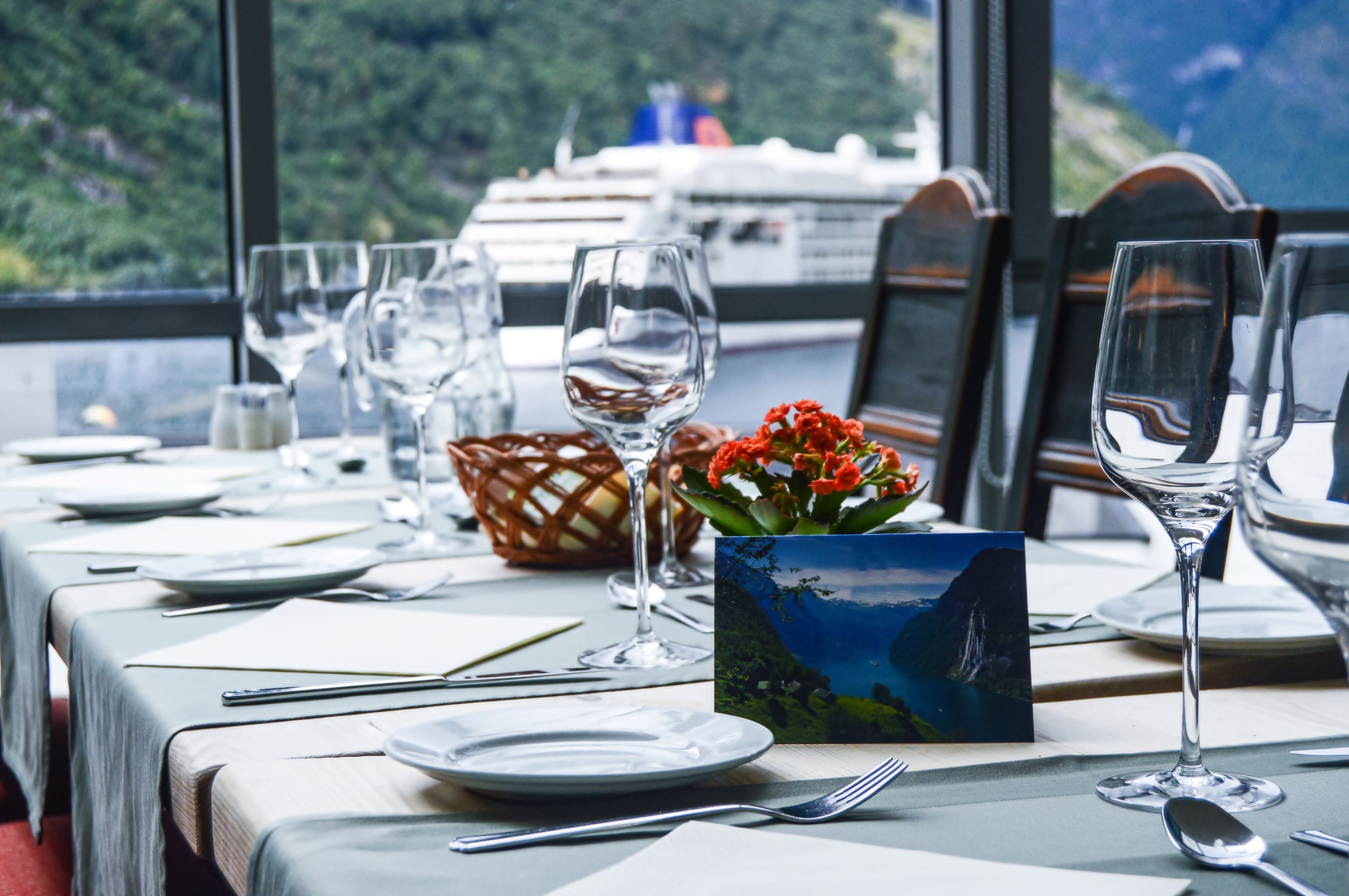 Elegant river cruise dining room with panoramic windows, fine table settings, and scenic fjord views beside a docked cruise ship.