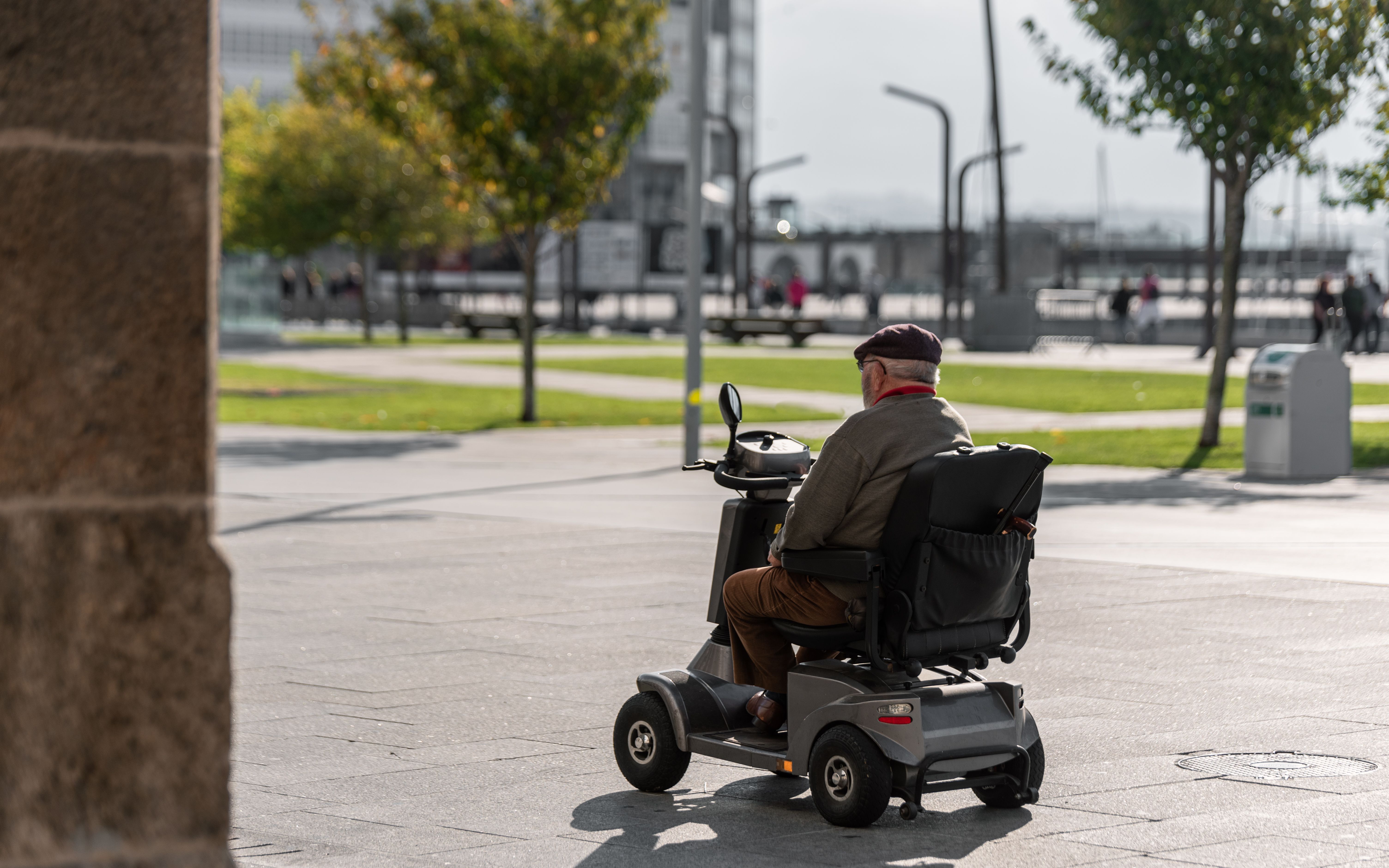 Elderly cruise traveler riding a mobility scooter along a waterfront promenade, highlighting accessible shore excursions and mobility-friendly cruise destinations.