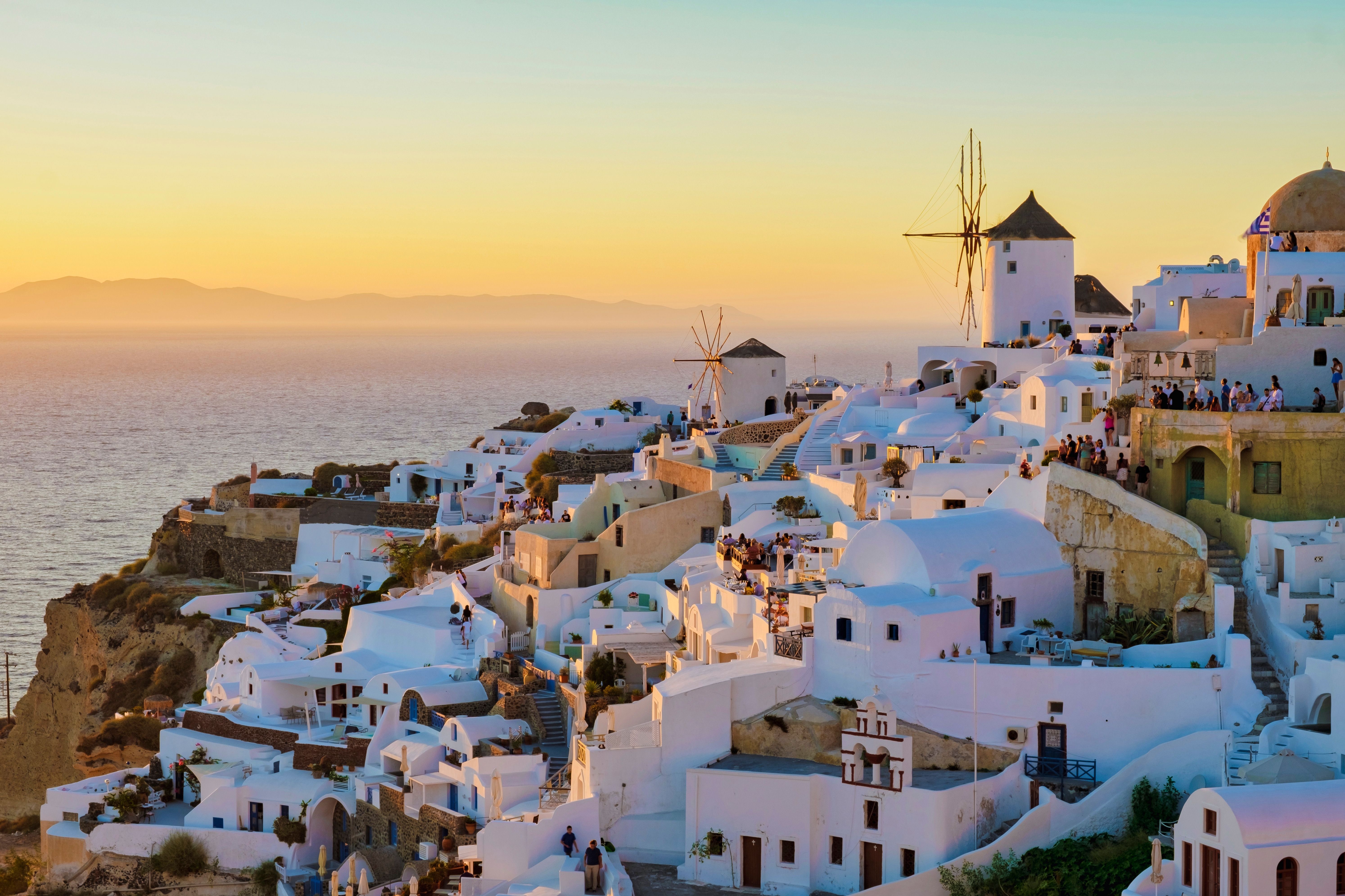 Villages of Santorini featuring Oia’s whitewashed homes, traditional windmills and cliffside architecture overlooking the Aegean Sea at sunset.