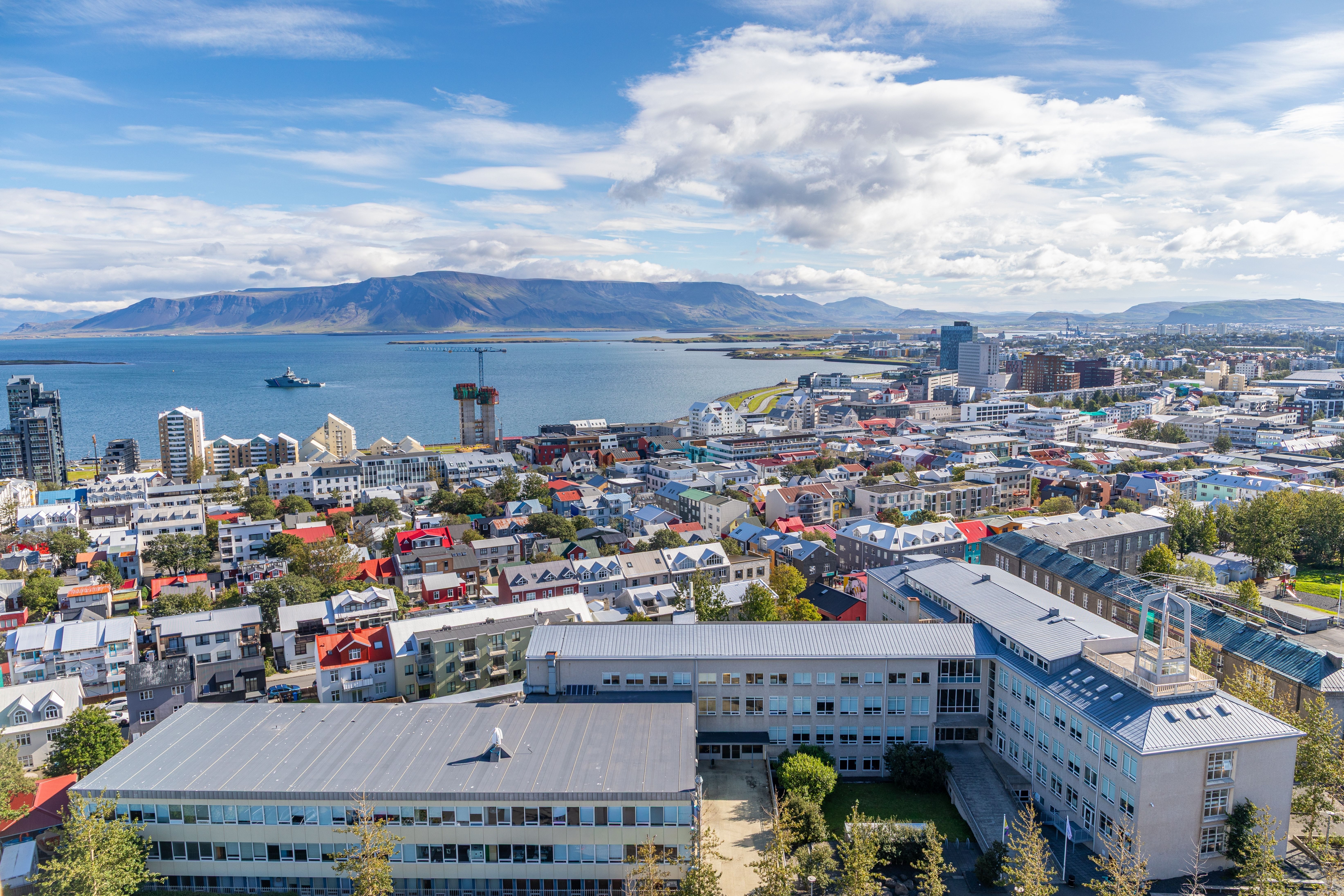 Panoramic Reykjavik cityscape overlooking Faxaflói Bay, colorful rooftops, modern waterfront districts, and Iceland’s scenic mountains near the cruise port.
